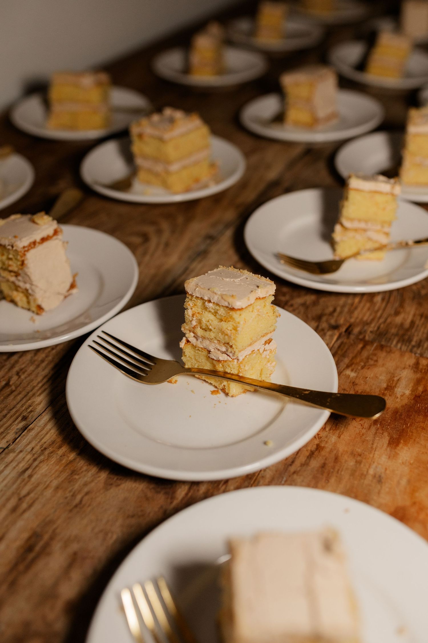 Multiple plates of layered vanilla cake served on a rustic wooden table at a wedding reception.