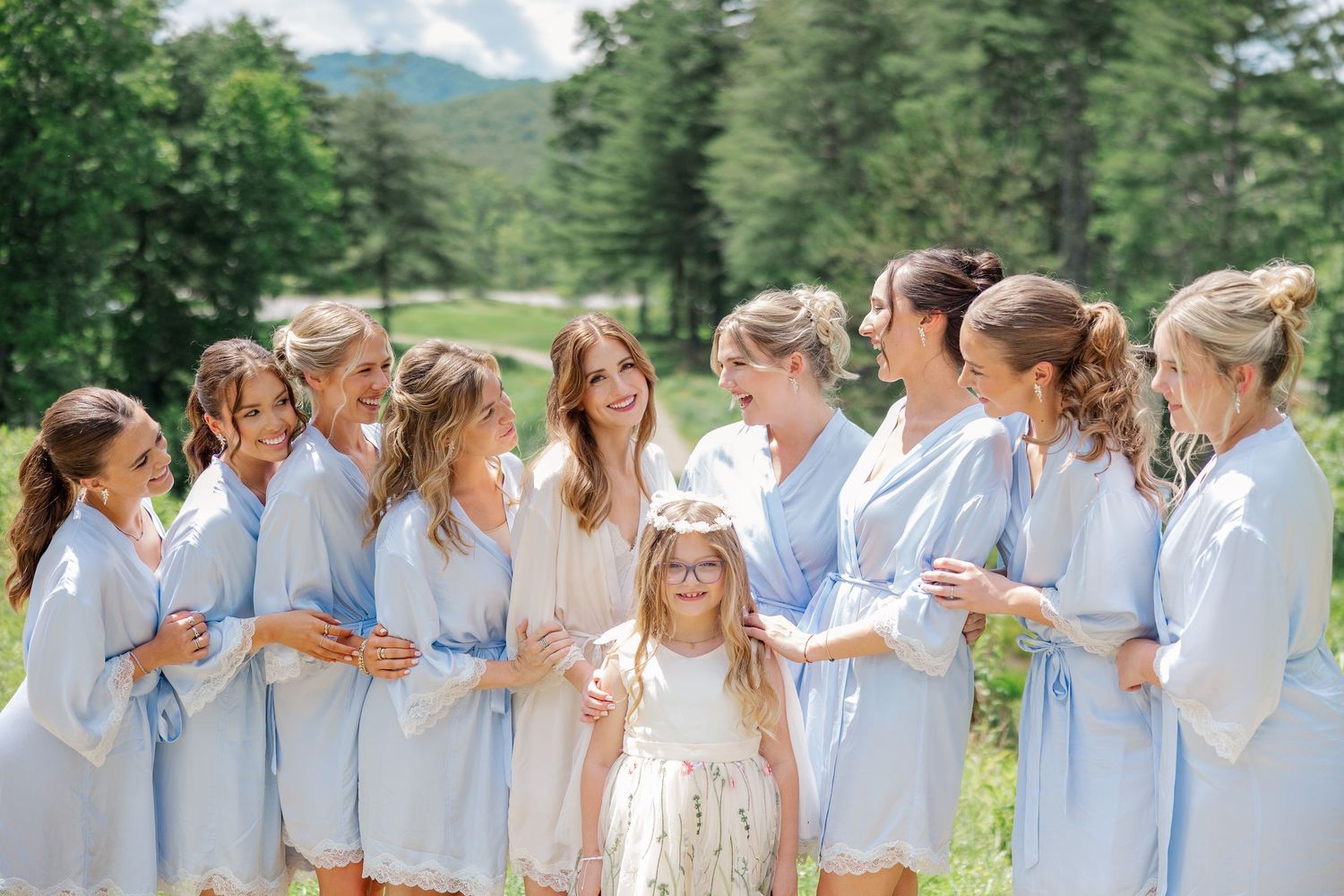 A line of people in light blue and white outfits standing together outdoors against a mountain backdrop.