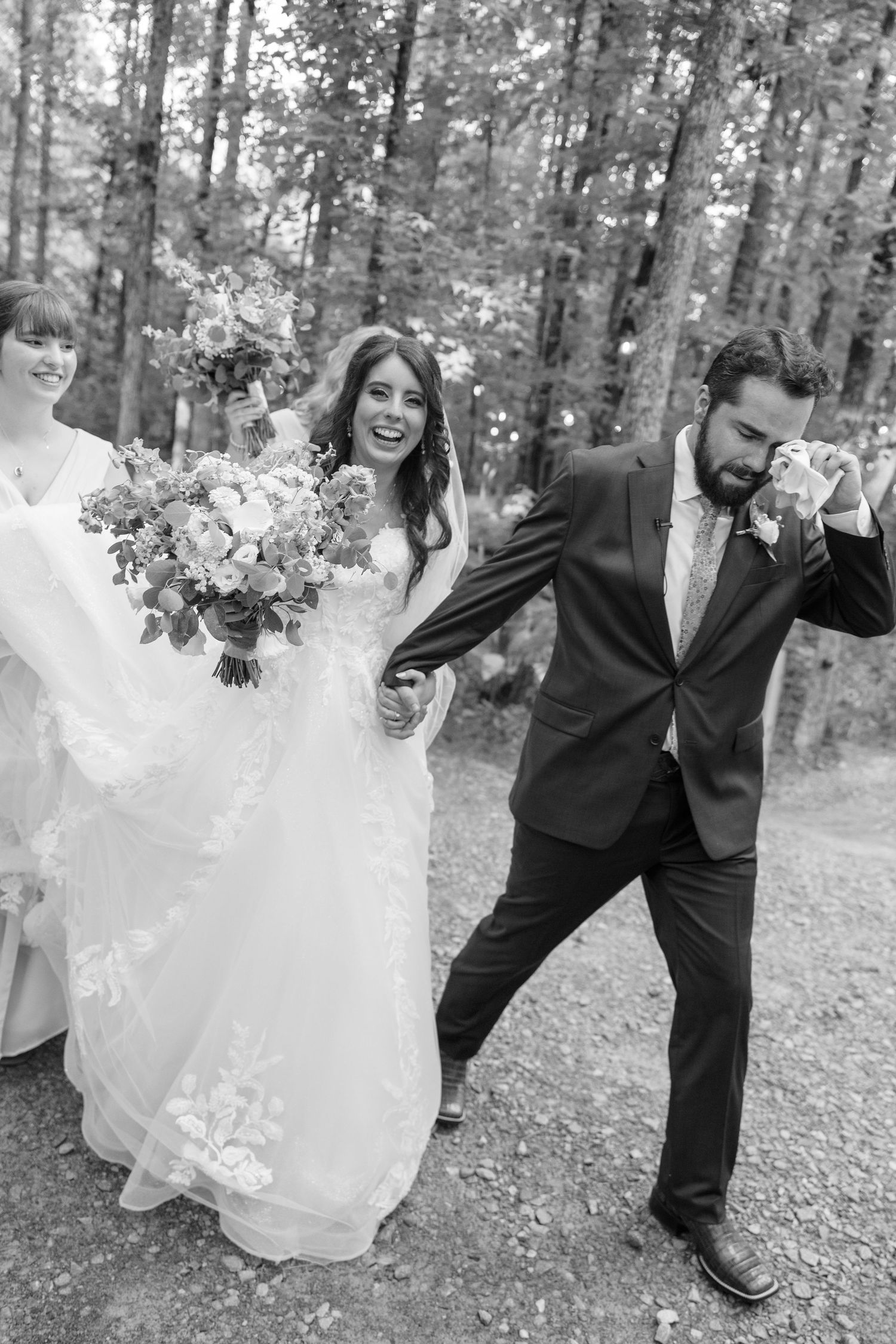 A joyous wedding party leaps playfully together on a woodland path during a photo session.