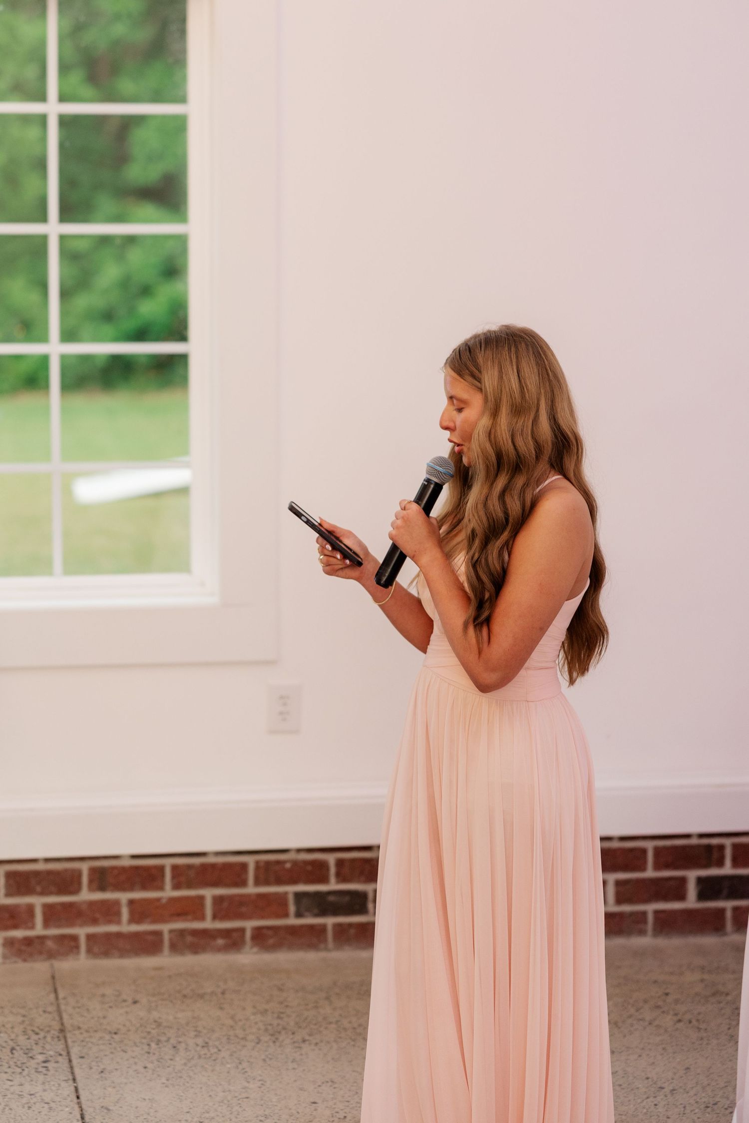 Bridesmaid in pink dress gives speech at wedding reception.