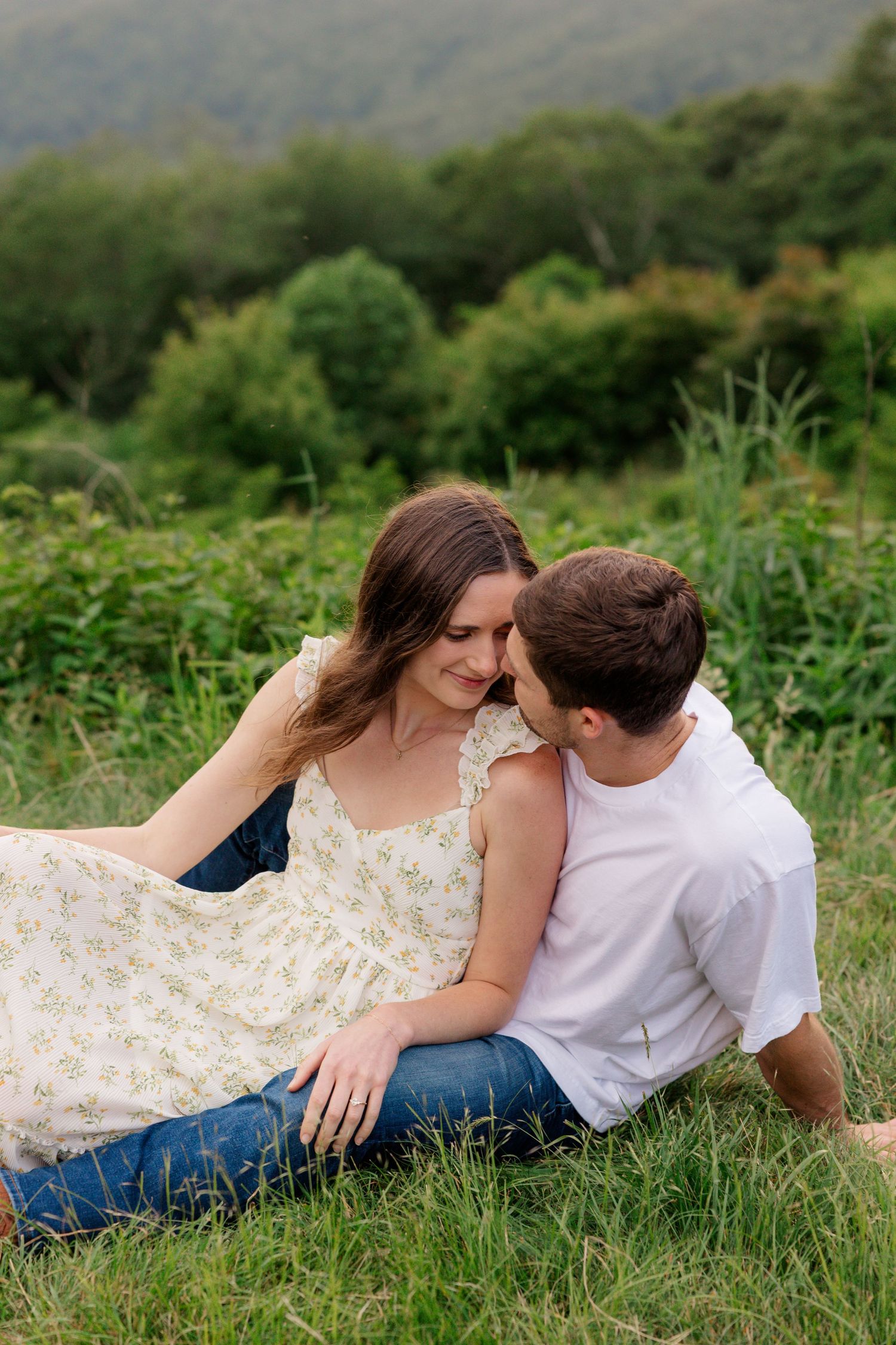 A romantic couple lounges in tall grass with mountains visible in the background.