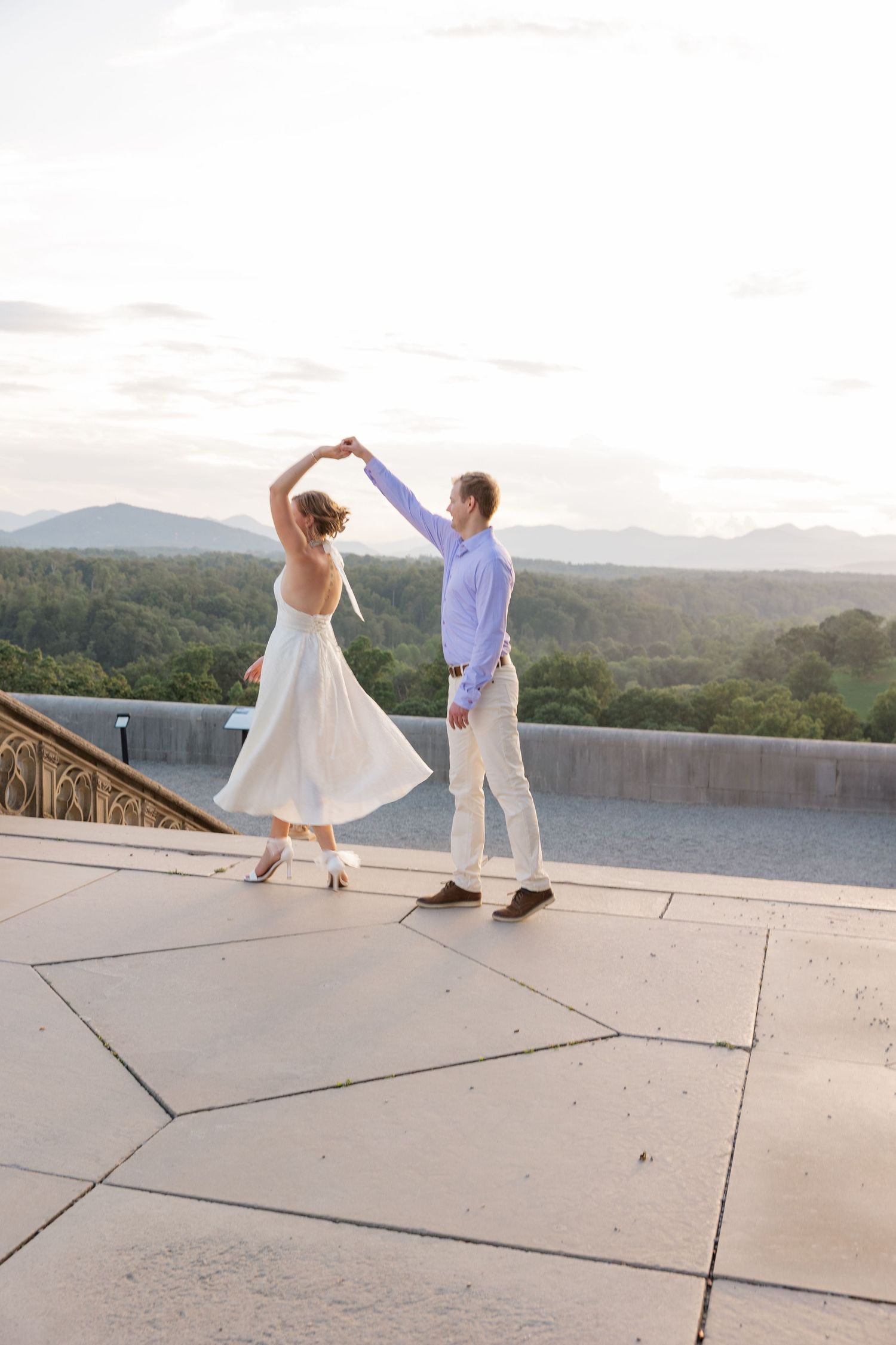 Couple dances together on a rooftop terrace overlooking scenic mountain views at sunset.