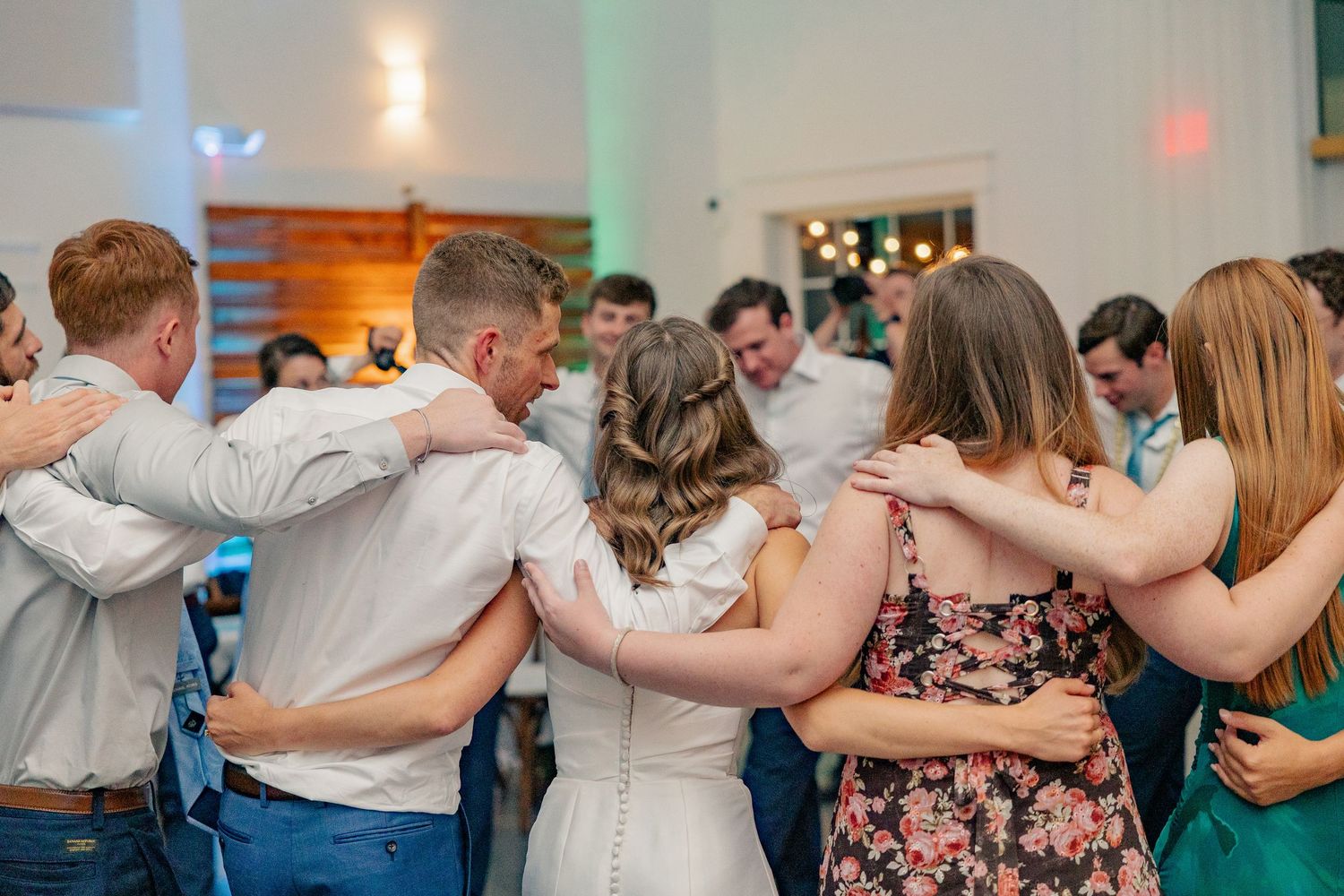Wedding guests form a circle with arms around each other dancing together on the reception dance floor.