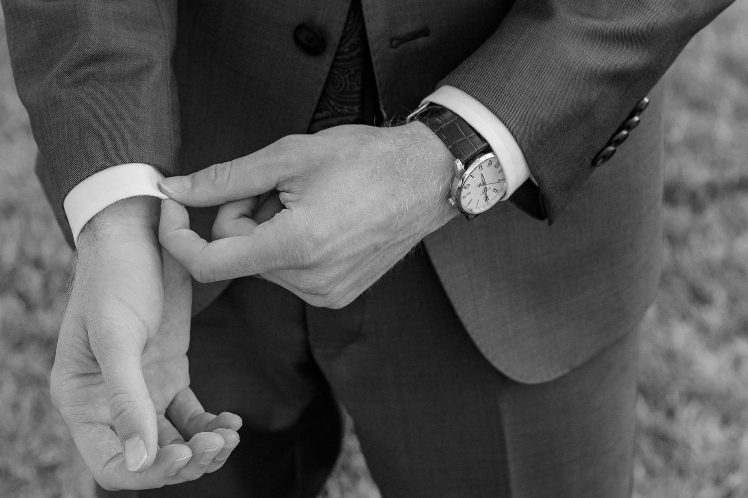 Groom adjusting his cufflinks wearing a classic watch and dark suit in a black and white wedding photo.