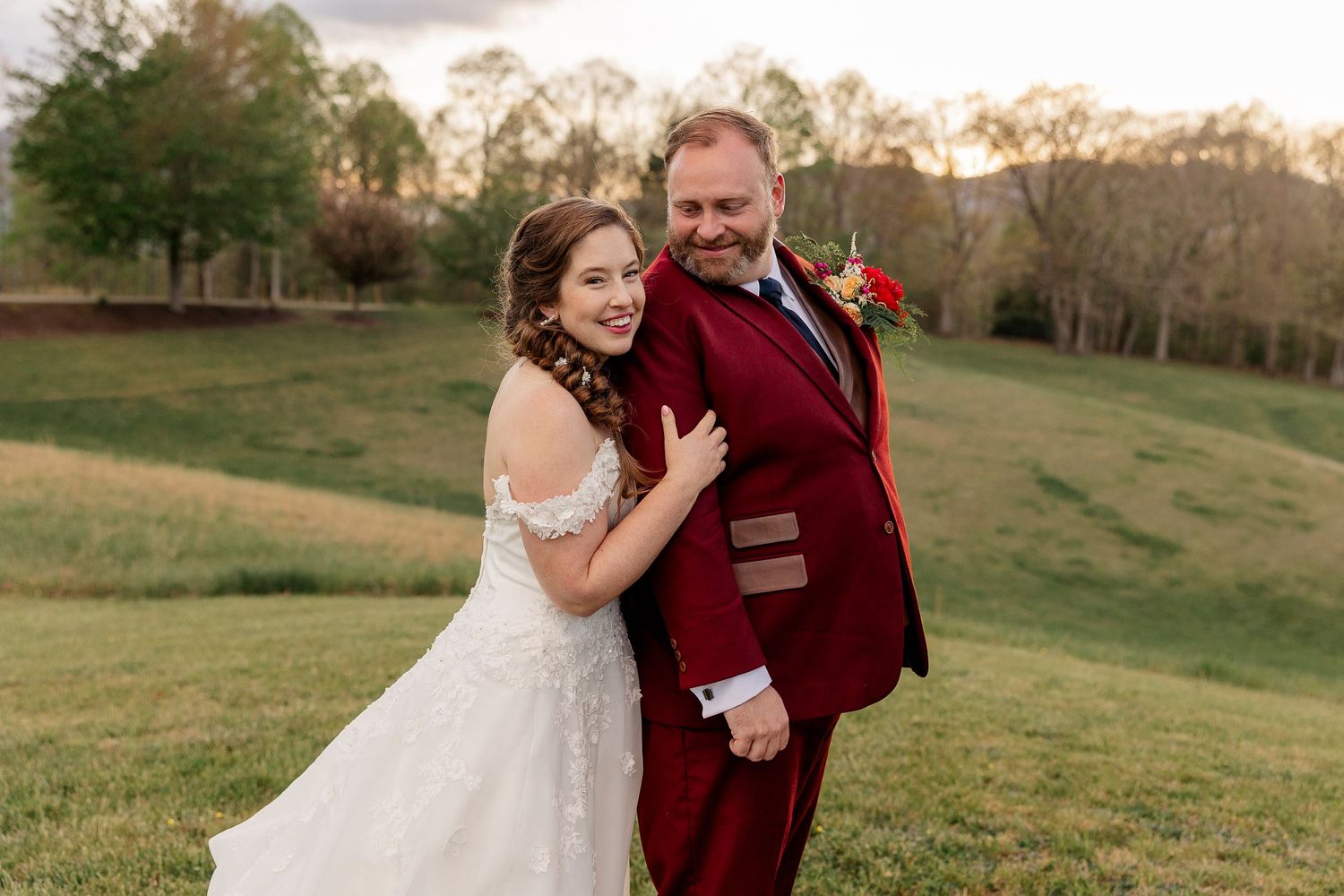 Couple celebrates their wedding at sunset in a burgundy and white themed outdoor ceremony in a grassy field.