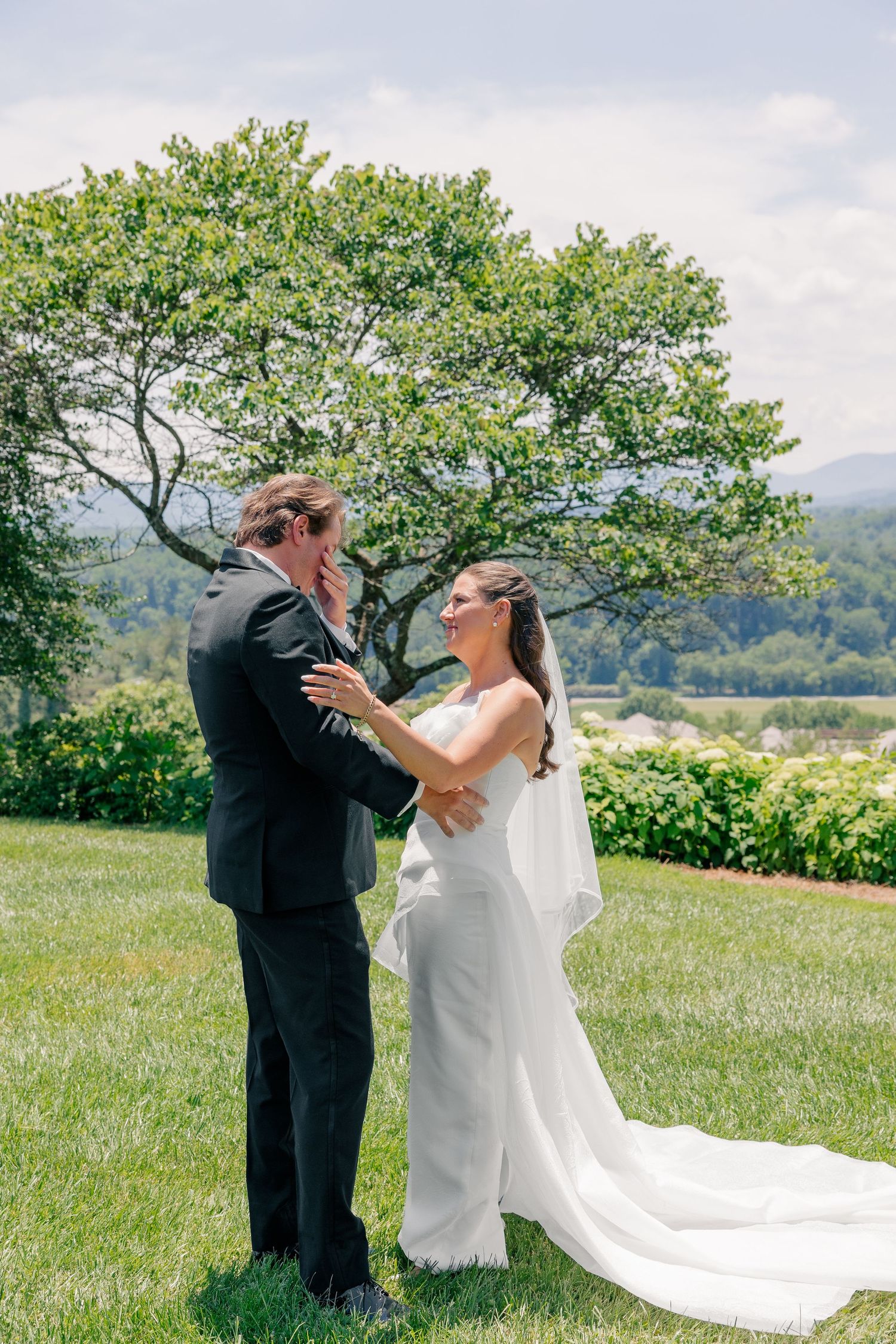 Bride and groom share first look moment on green lawn with scenic mountain views.