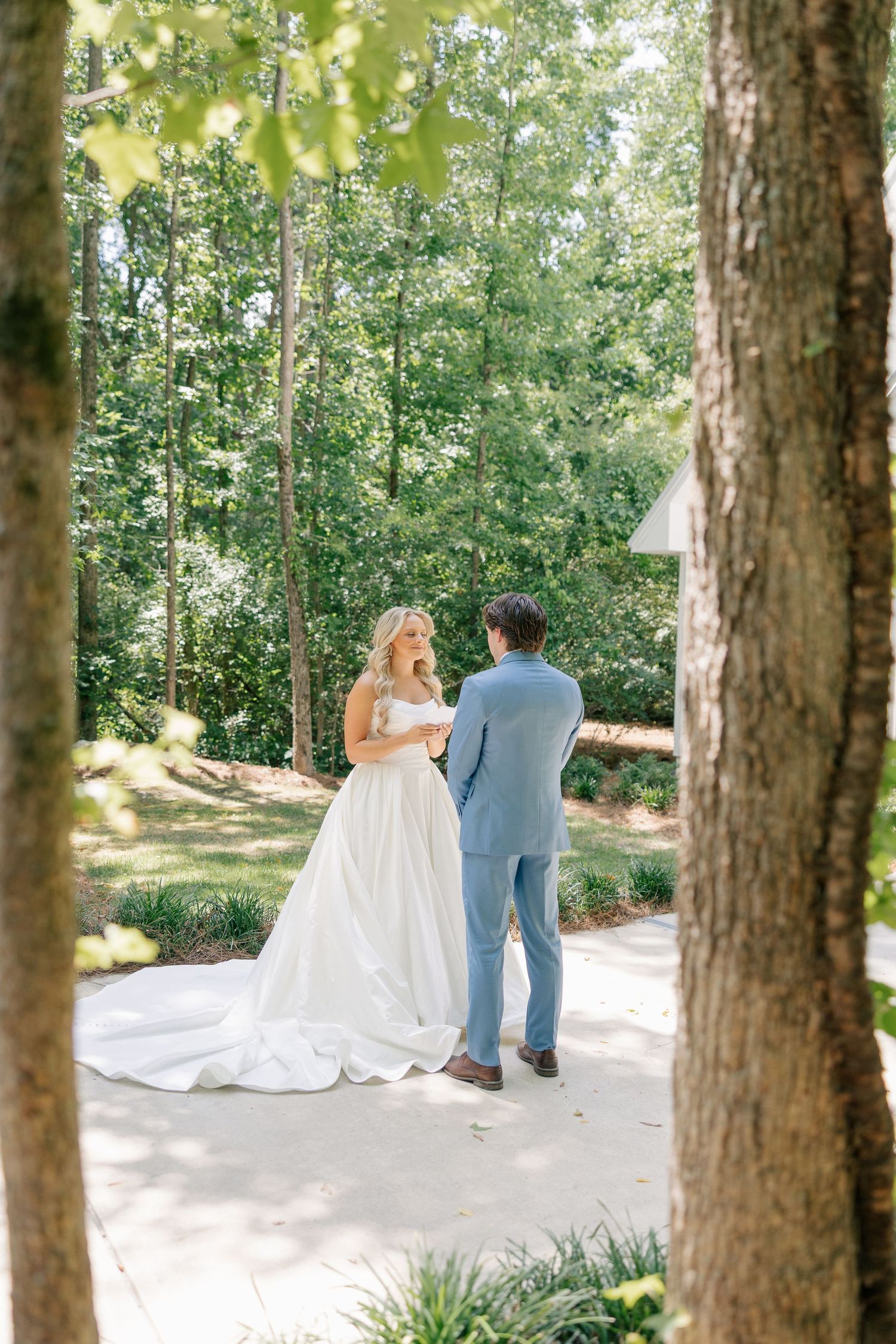 Bride and groom exchanging vows outdoors framed by trees in a garden setting.