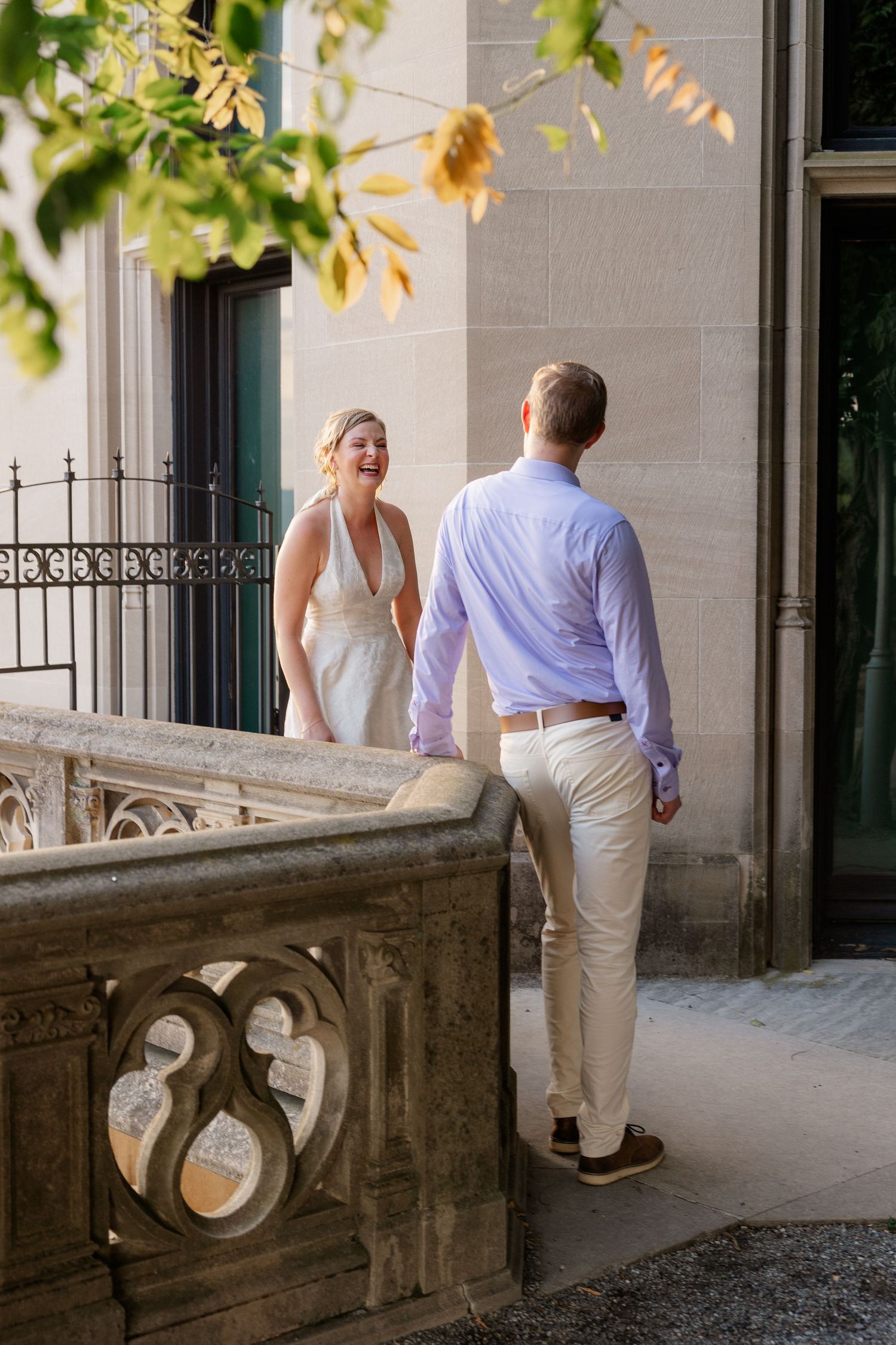 A couple walks along an elegant stone balcony with ornate architectural details.