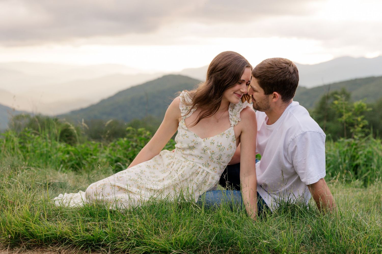Two people share an intimate dance pose in a scenic mountain field during golden hour.