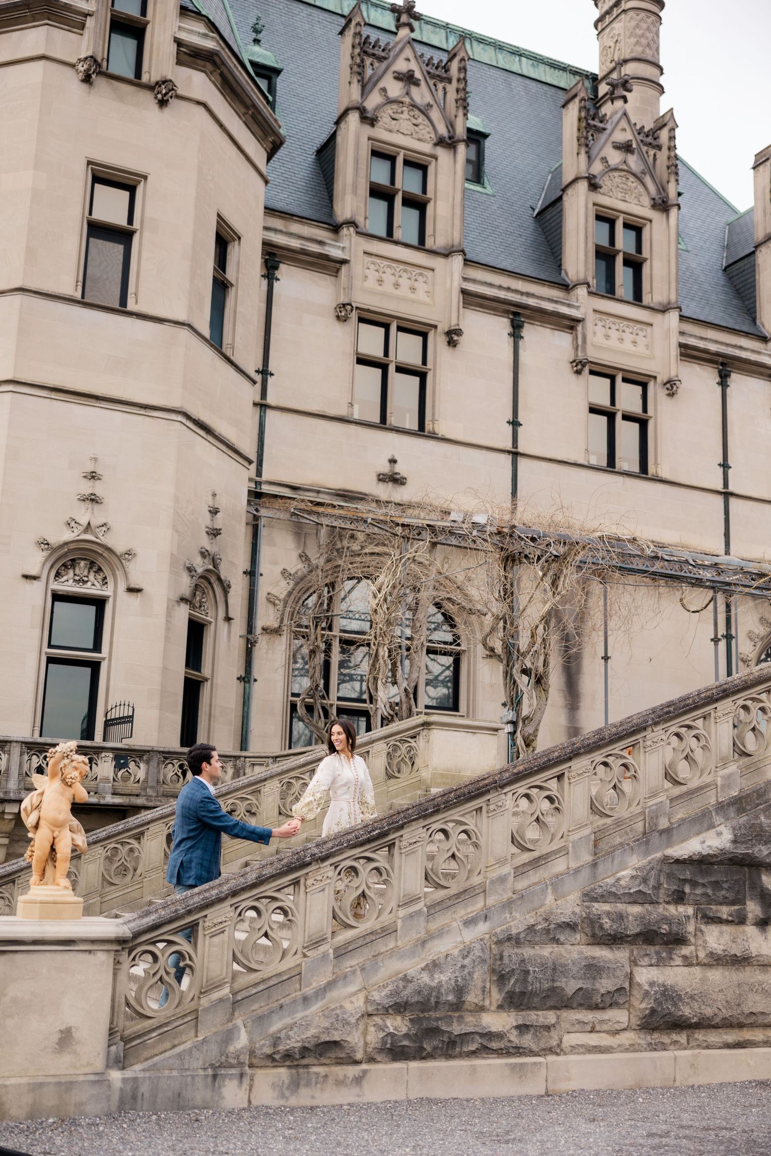 A grand staircase leads to the entrance of Biltmore Estate with its Gothic Revival architecture and ornate stone details.