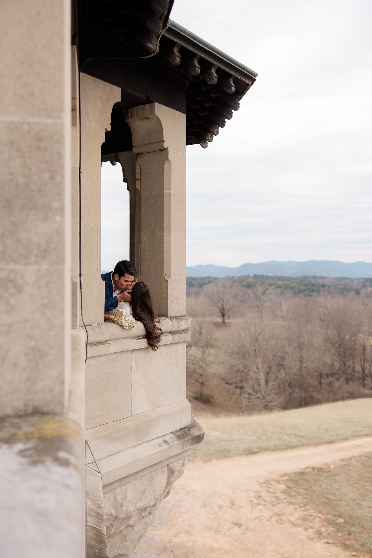 Person perched in stone archway of historic building overlooking mountainous winter landscape at sunset.