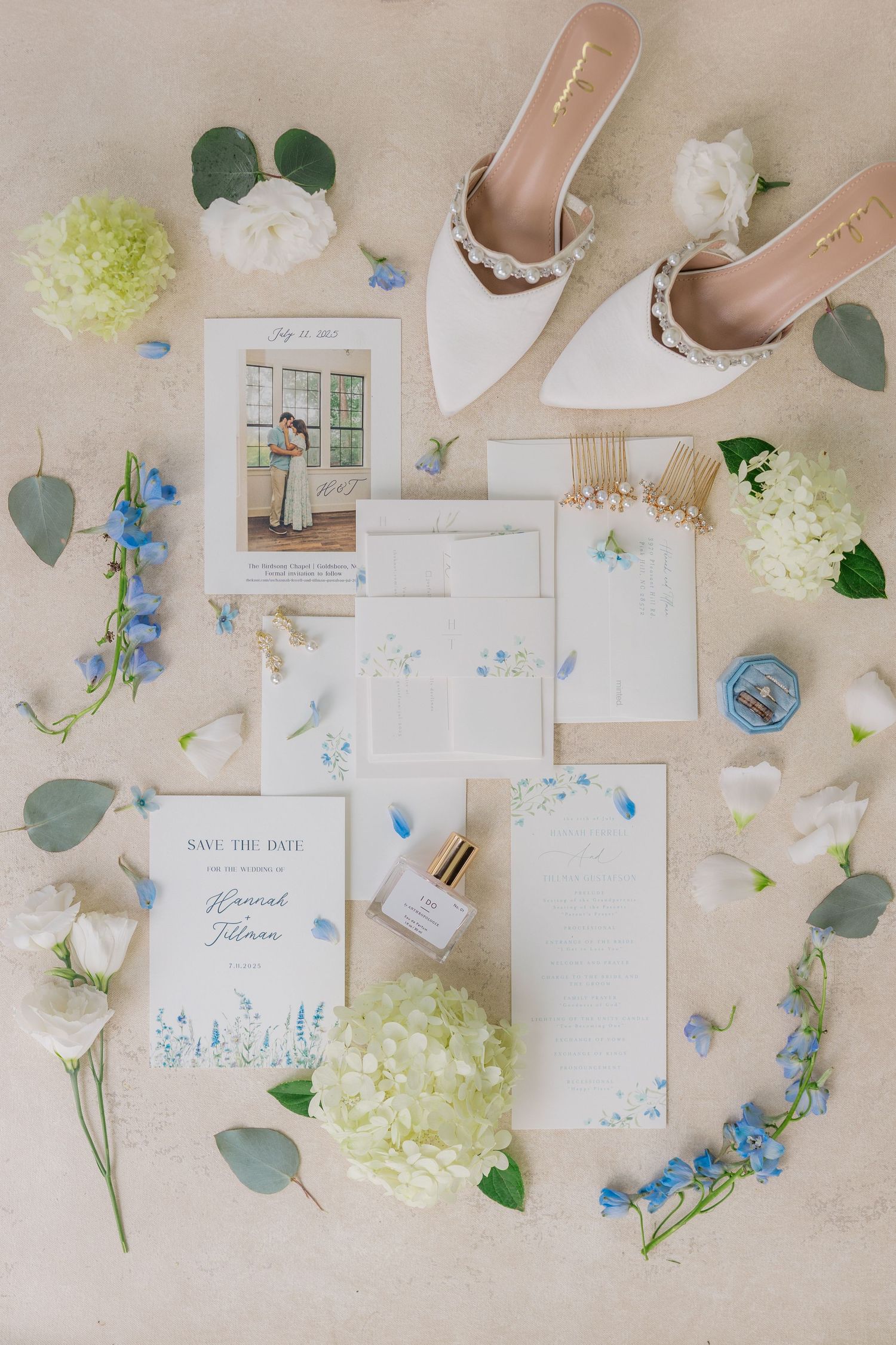 Elegant wedding stationery flatlay with blue and white florals, featuring save the dates and delicate eucalyptus leaves.