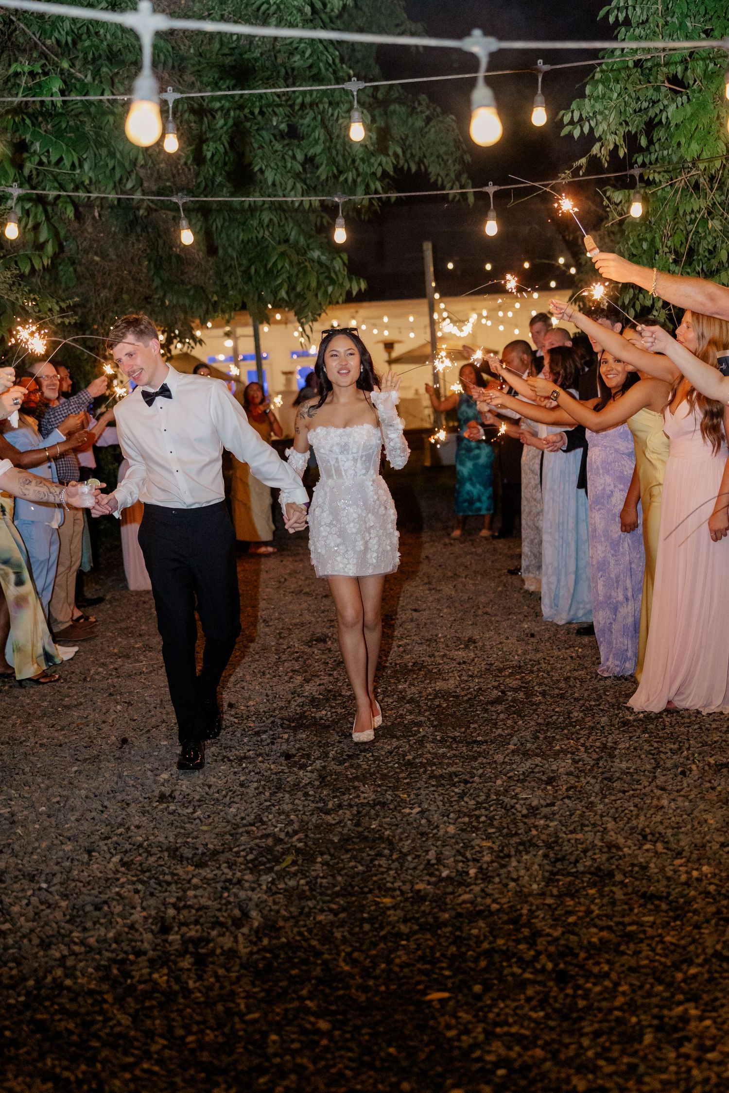 Wedding guests dance under string lights at an outdoor evening reception.