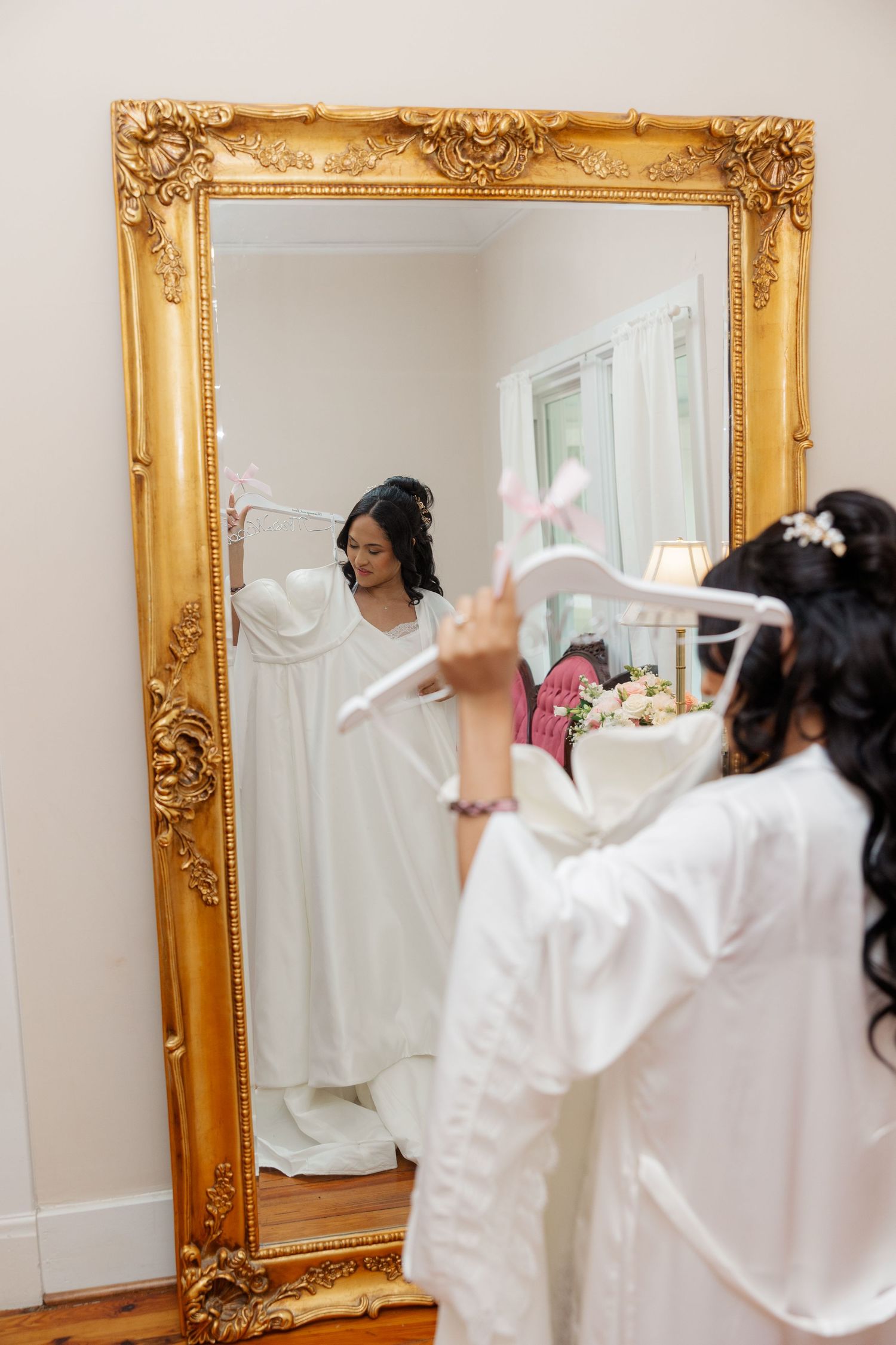 Ornate gold-framed mirror reflecting wedding day preparations with white robes.