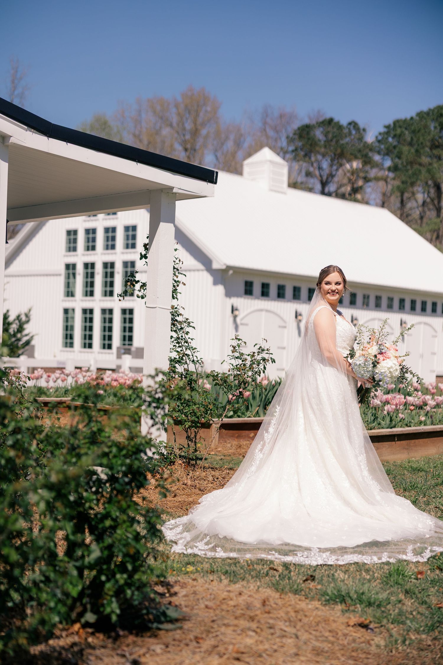 A dramatic wedding dress train extends across landscaped grounds with white buildings in the background.