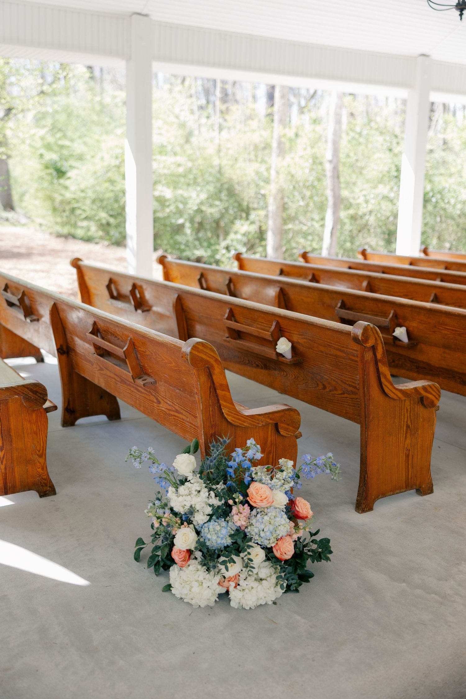 Wooden church pews decorated with pale pink and white floral arrangements in a bright chapel.