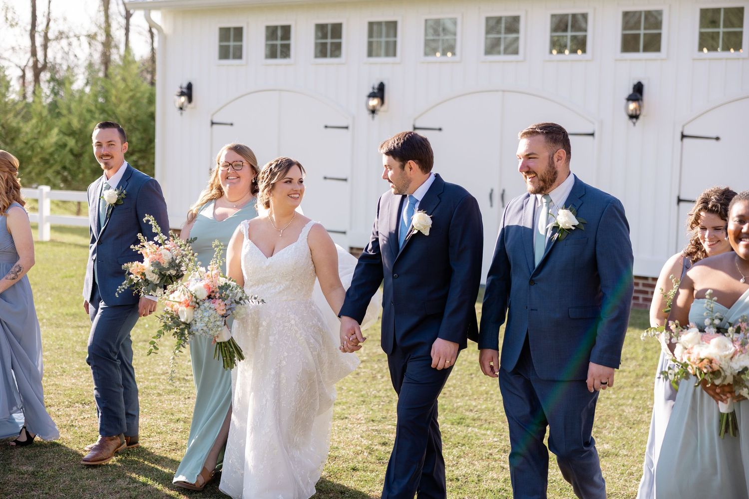 Wedding party in blue and gray attire poses together against white building.