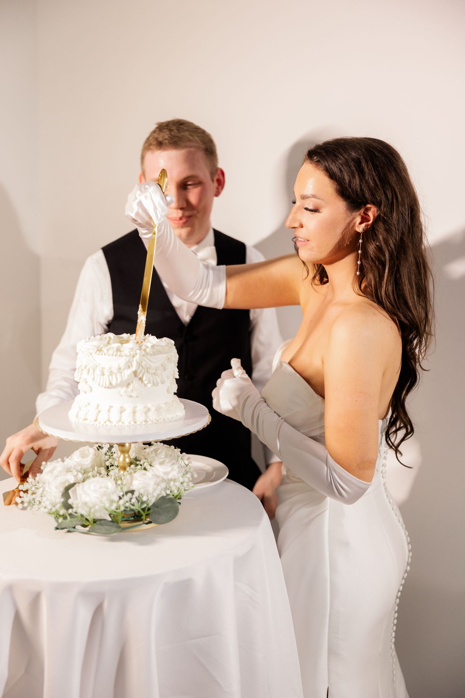 Wedding couple sharing cake and laughing together at reception table with white tablecloth.