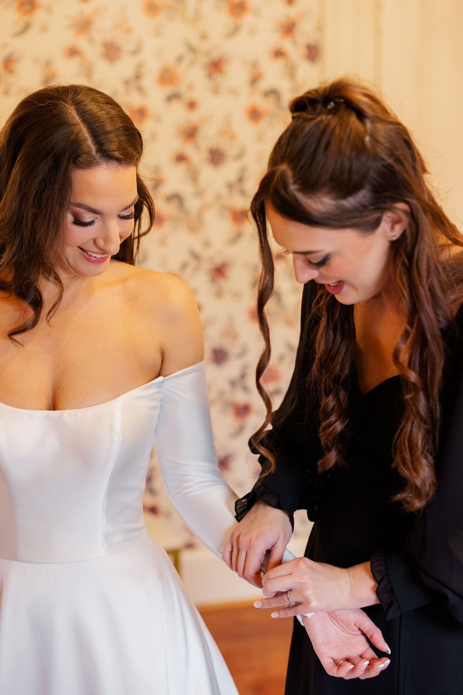 A bride in a white off-shoulder dress getting final adjustments to her attire.