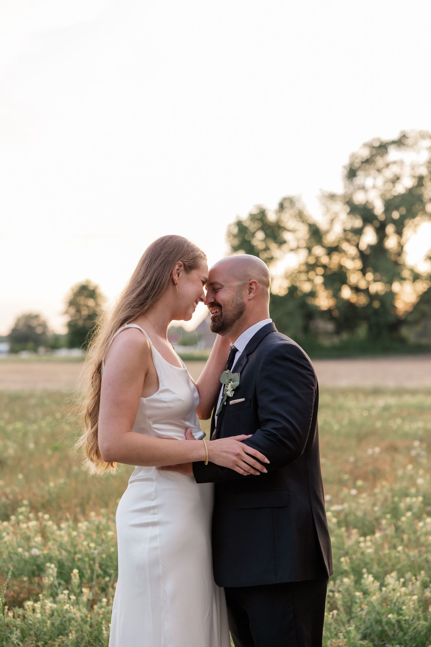 A tender moment between a couple in wedding attire standing in a wildflower field at dusk.