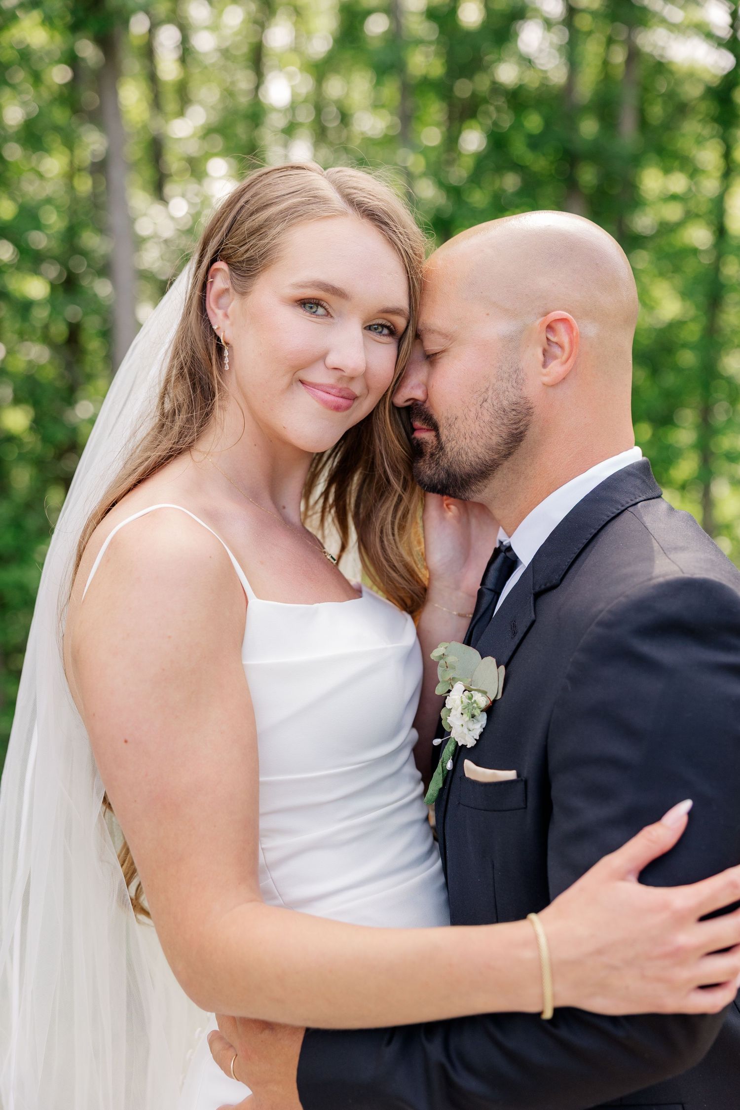 Tender wedding portraits of couple embracing in sunlit garden setting.