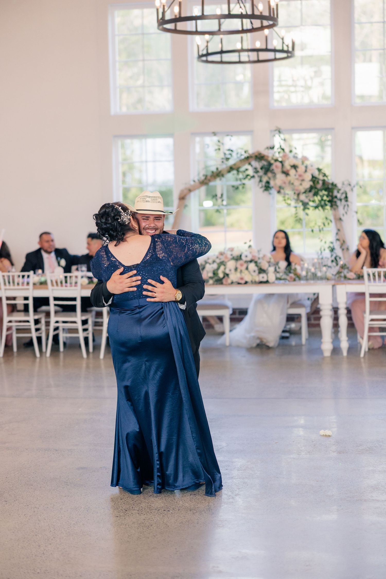 Wedding guests dancing together in navy blue attire at elegant reception venue with chandeliers.