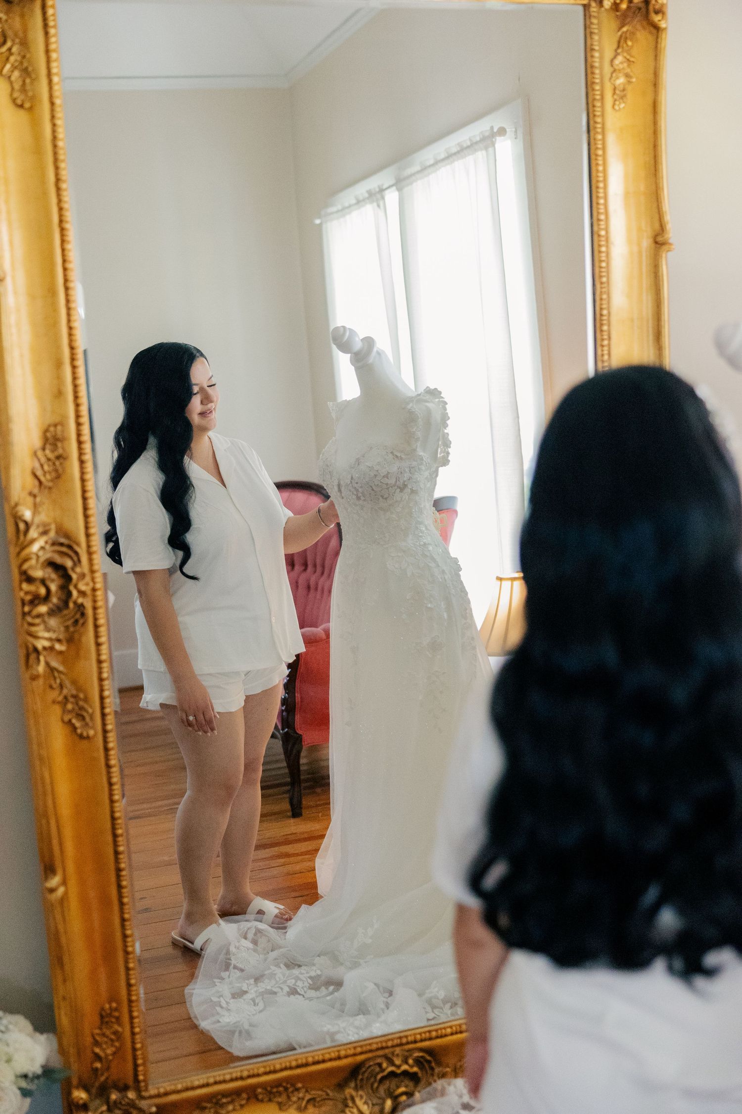 Elegant gold-framed mirror reflects a traditional bridal gown being fitted.