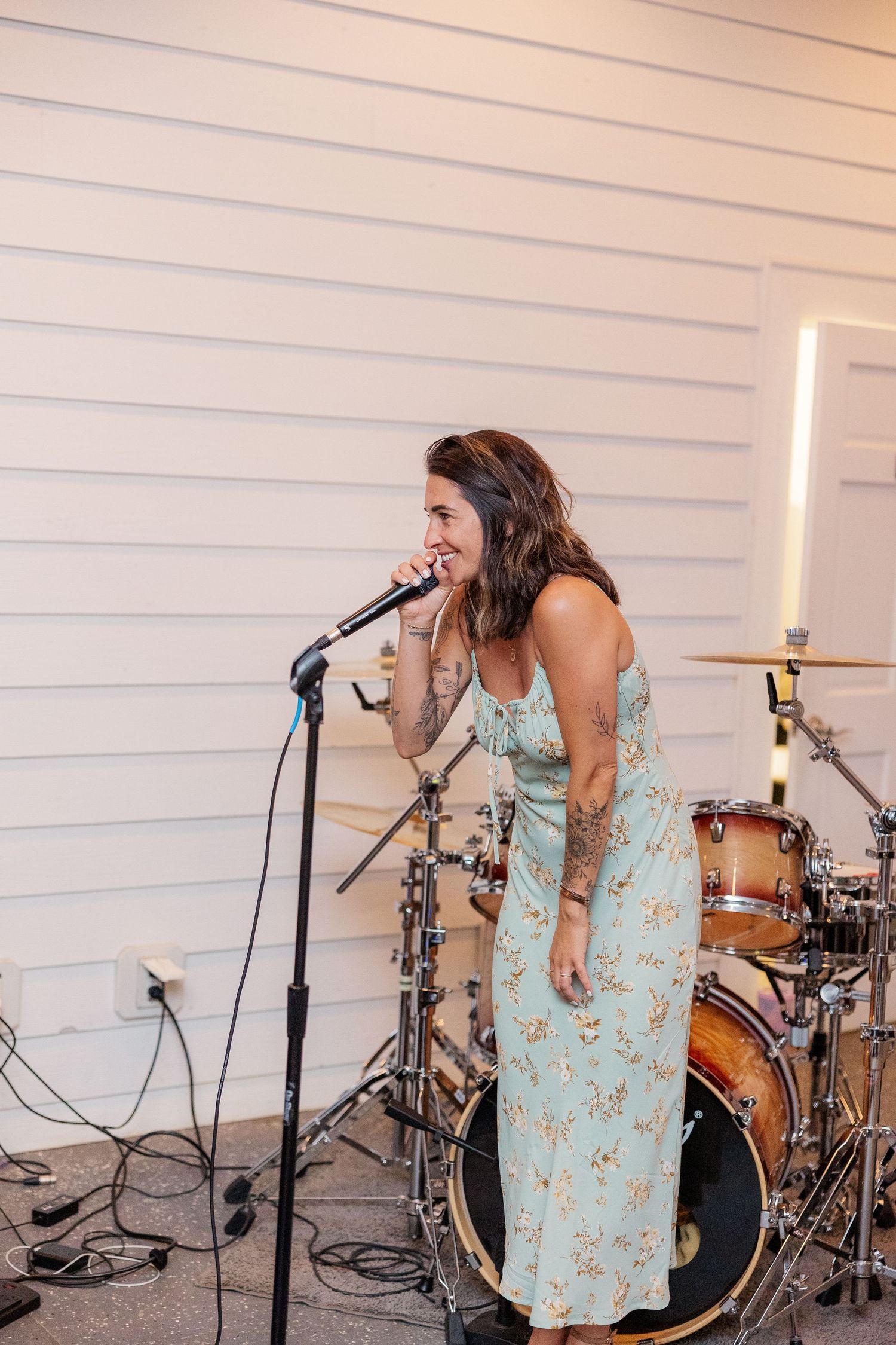 Musical performance setup with microphone and drum kit against white shiplap walls.