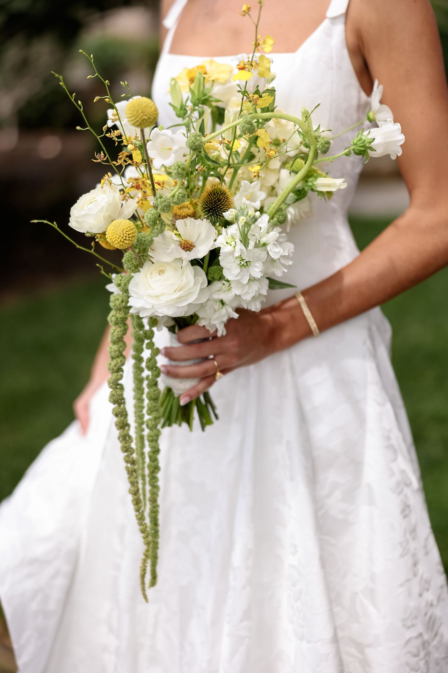 Bride in white lace dress holding wildflower bouquet with white ranunculus and yellow billy balls.
