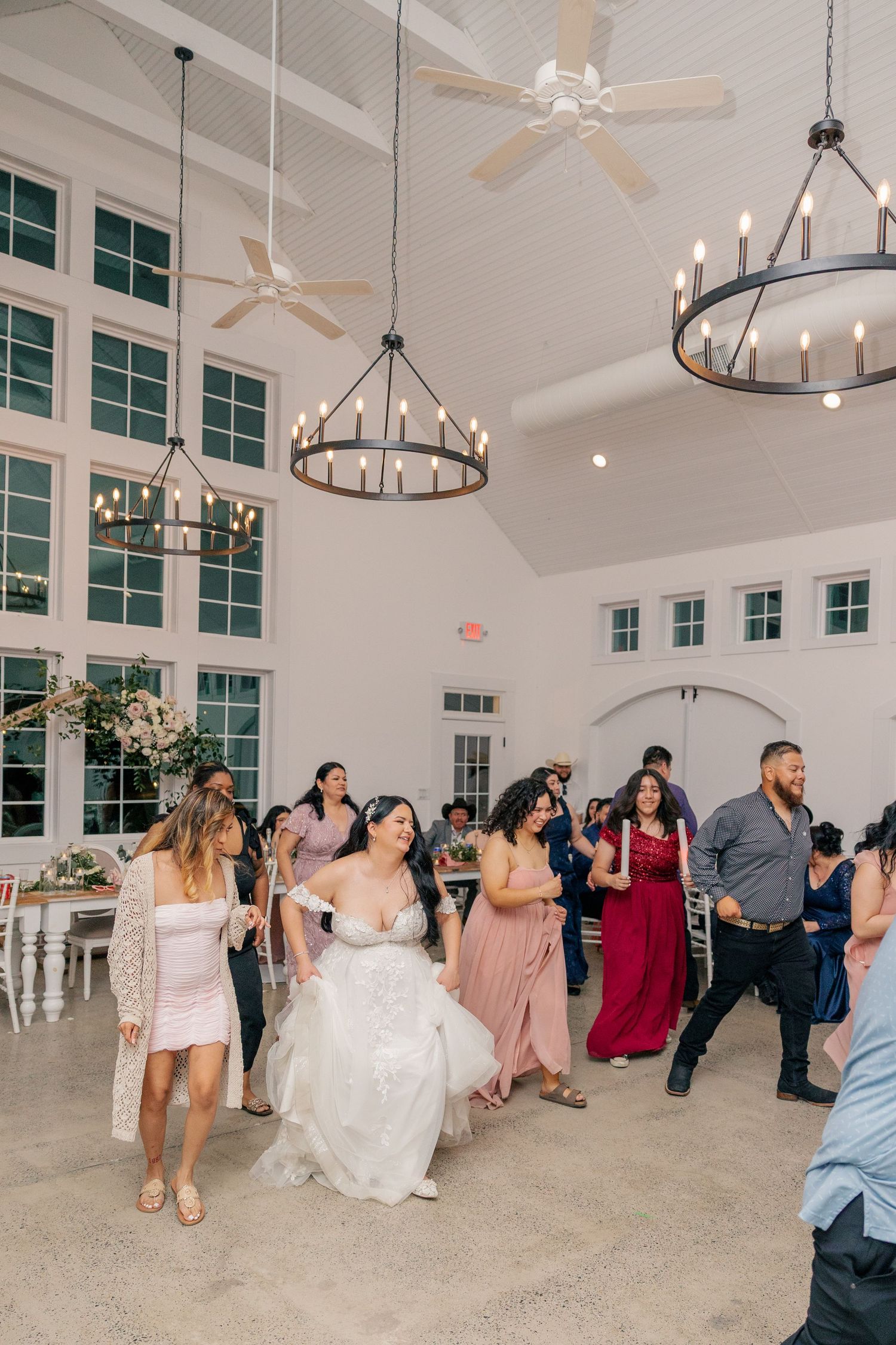 Wedding guests dancing and celebrating in a modern white reception venue with vaulted ceilings.