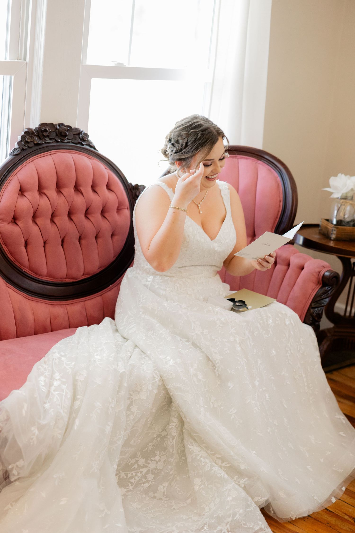 A bride in an elegant white gown reclines on a pink tufted sofa.