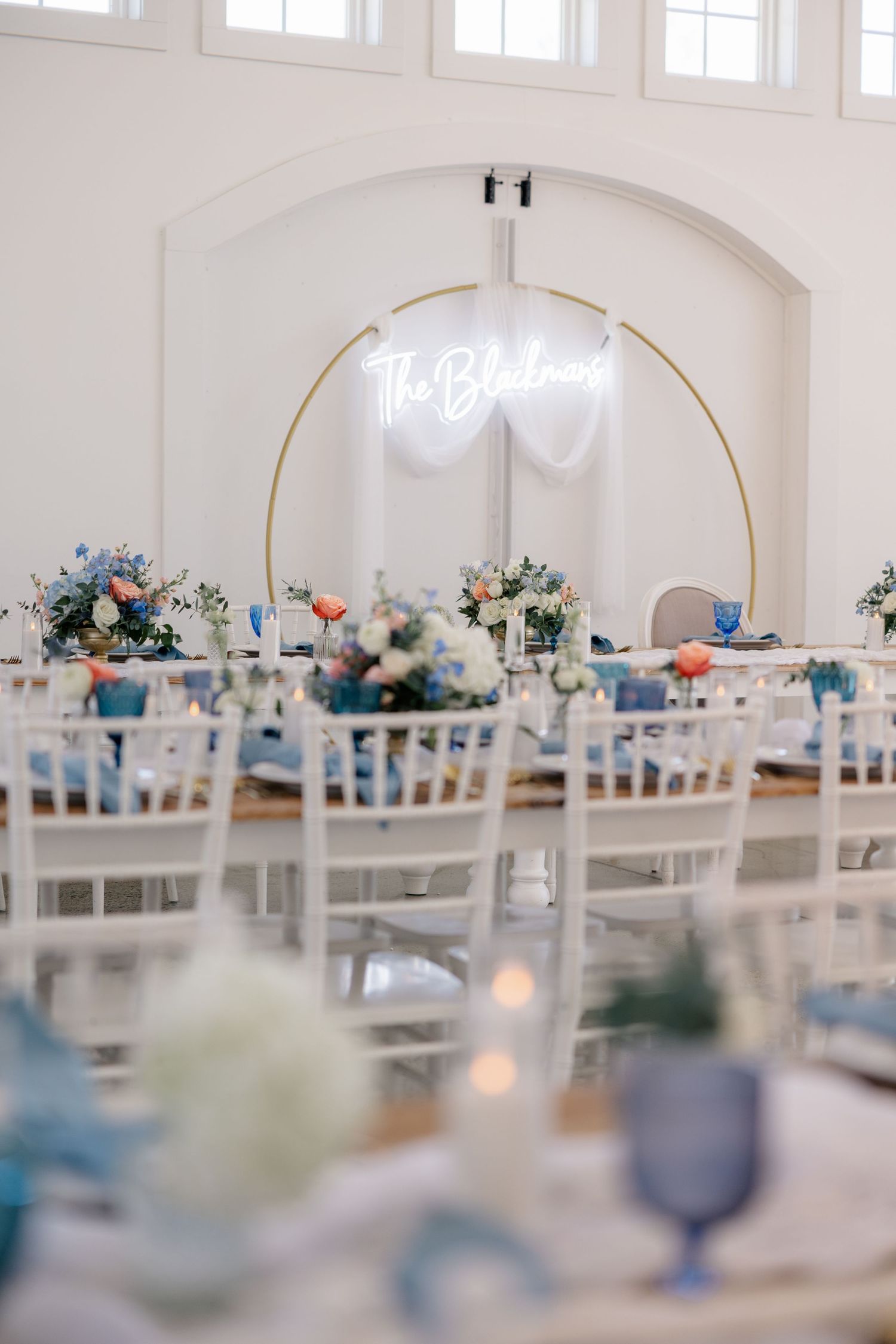 Elegant white wedding reception room with tables set for dinner and blue floral decor accents.
