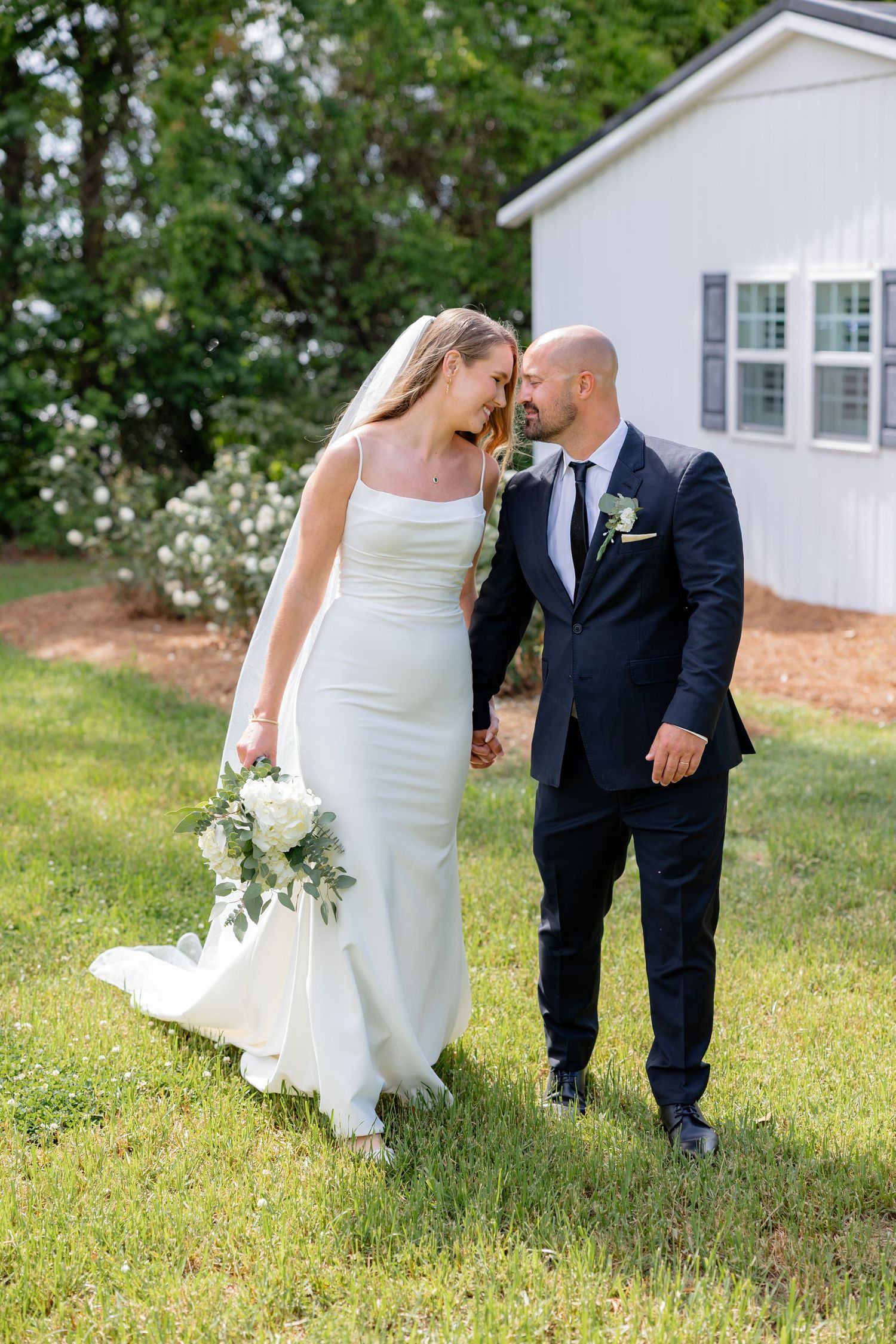 A romantic wedding moment captured in a garden setting with white floral bouquet.