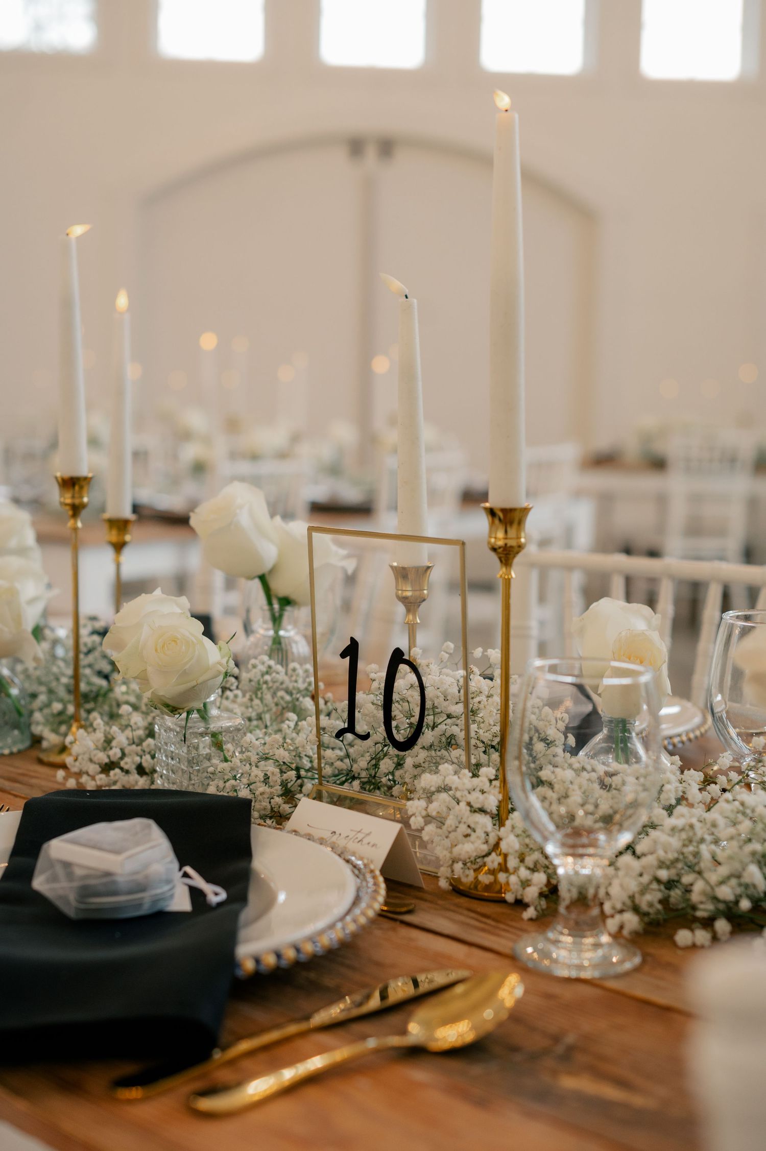 Wedding reception table details with white candles, flowers and table numbers on a rustic wooden surface.