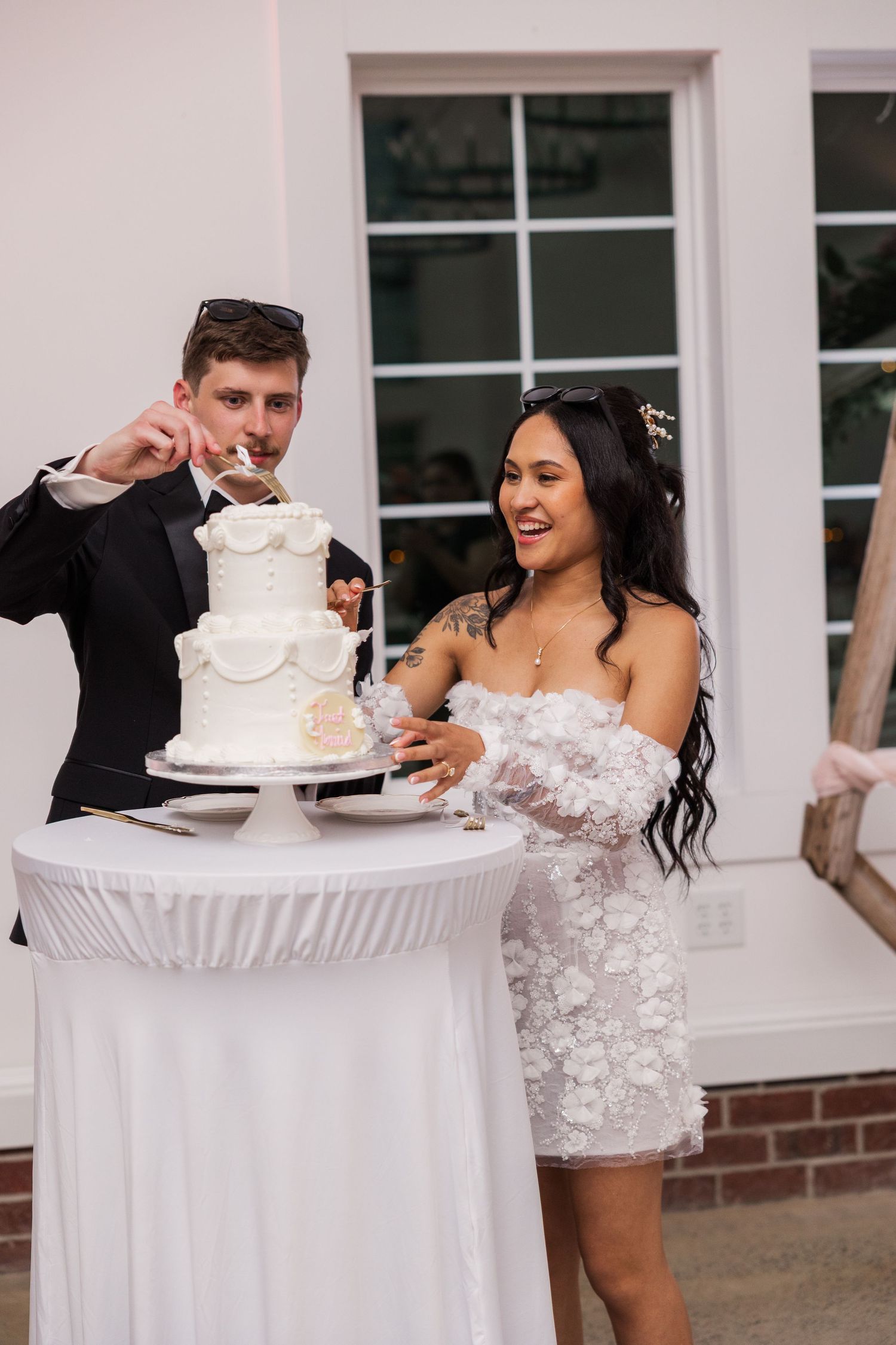 Newlyweds share a lighthearted moment while cutting their white tiered wedding cake.