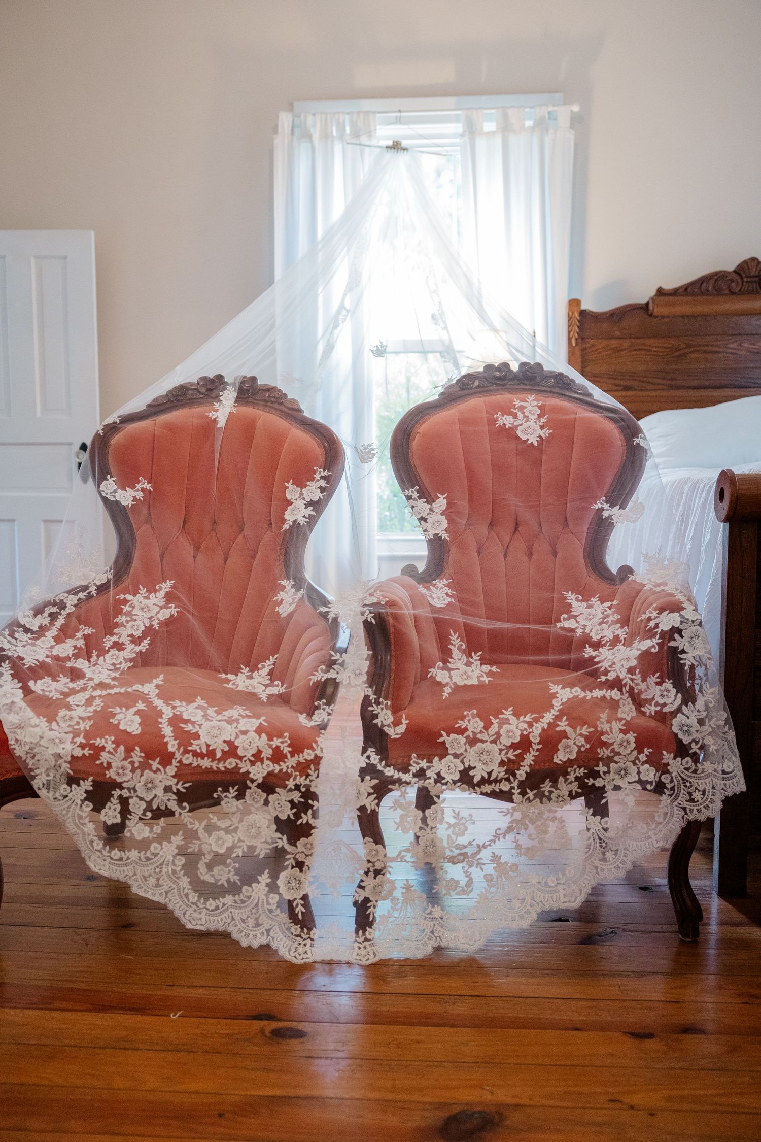 A delicate white lace veil draped over pink vintage chairs in a sunlit room.
