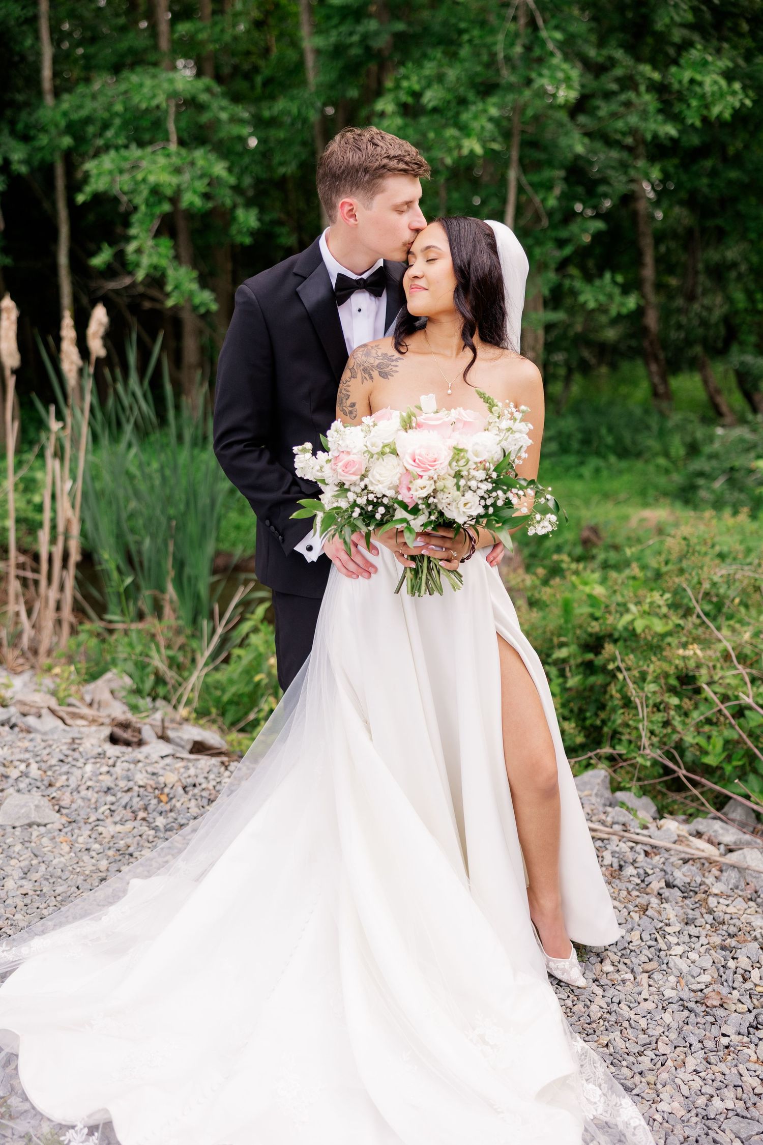 A romantic outdoor wedding photo with a flowing white gown and lush pink bouquet against a forest backdrop.