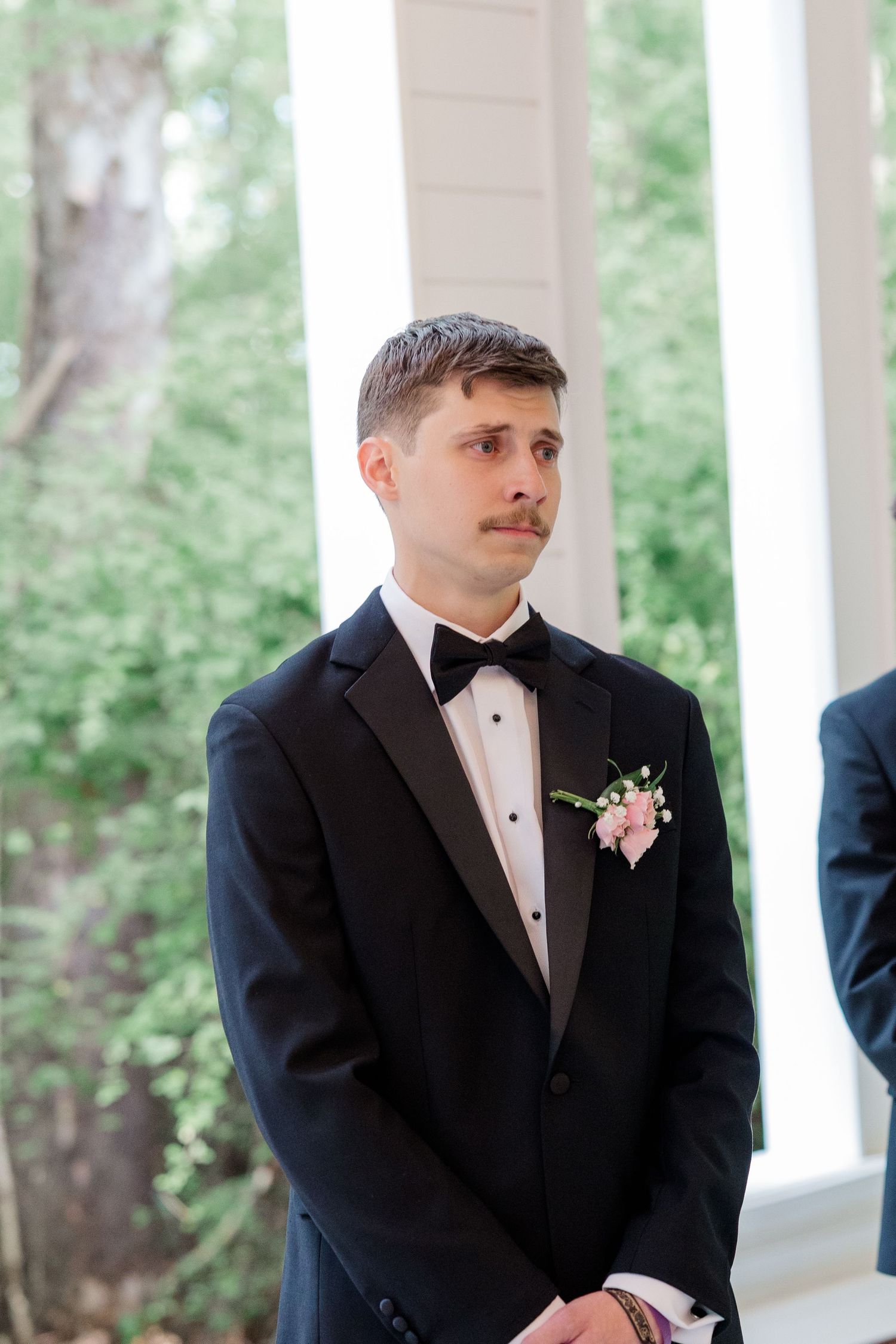 Classic black tuxedo look with boutonniere at an outdoor wedding ceremony.