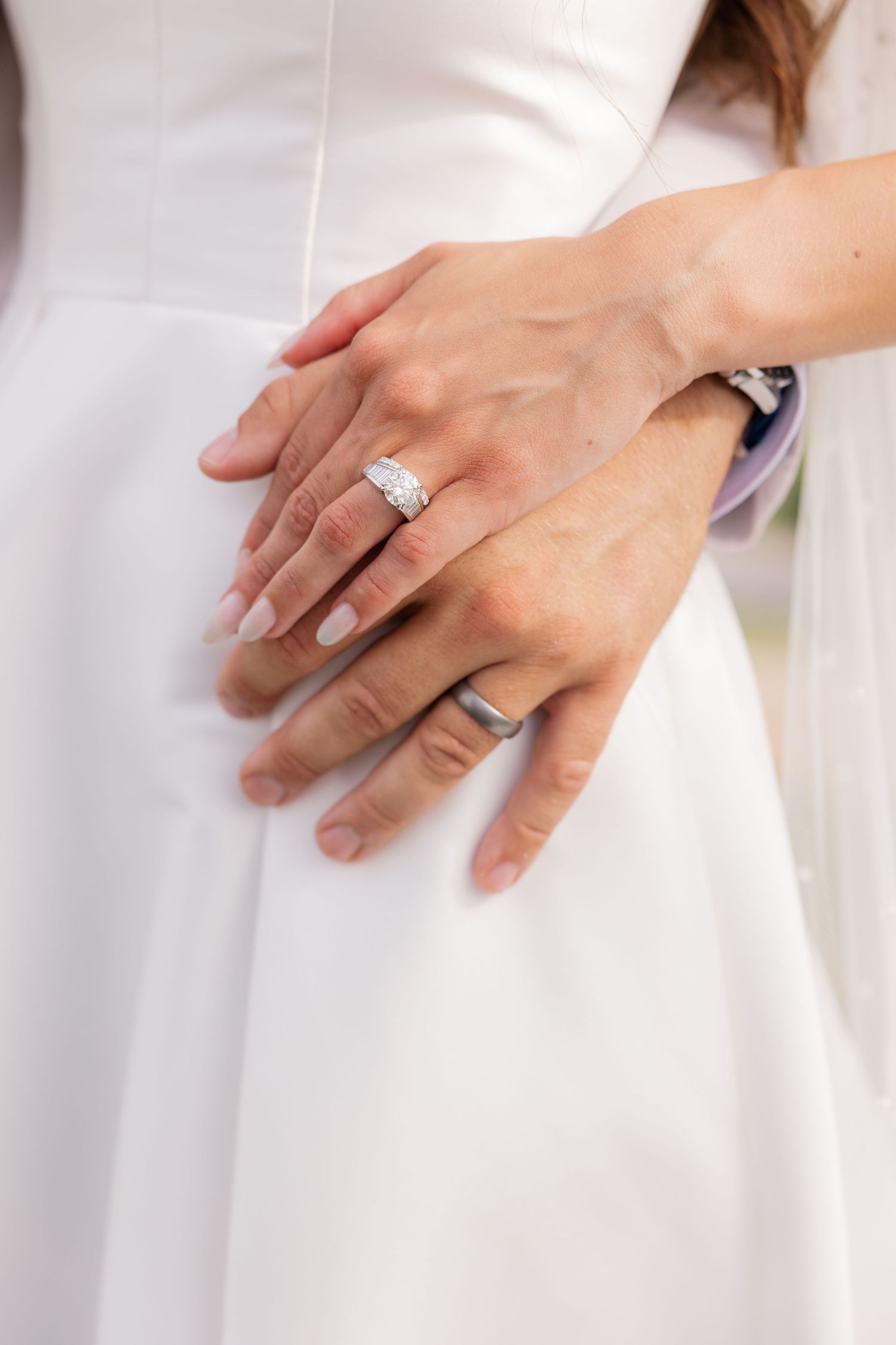 Close-up of hands showing wedding ring details on white dress fabric.