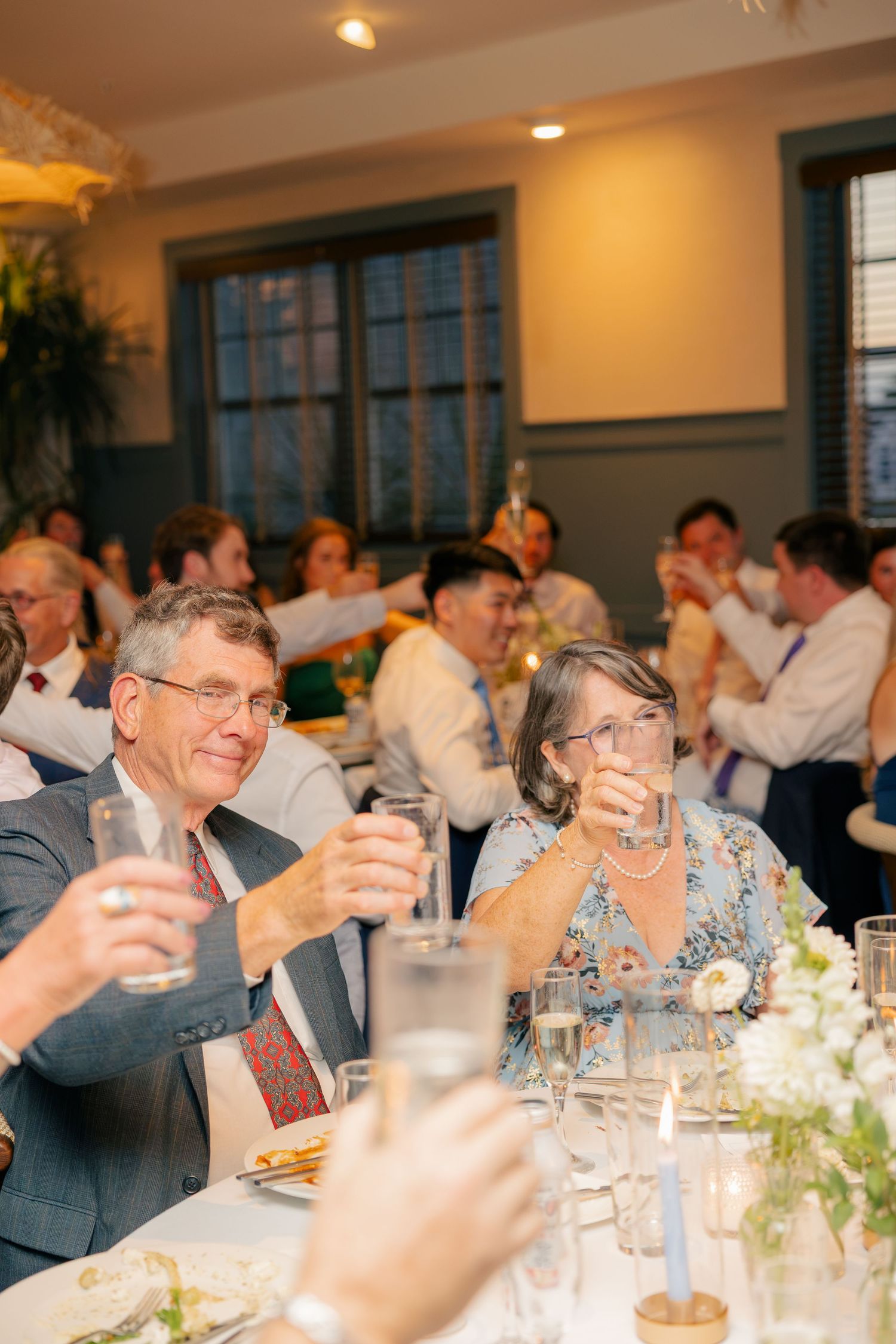 Wedding guests raising glasses in a toast during elegant indoor reception dinner celebration.