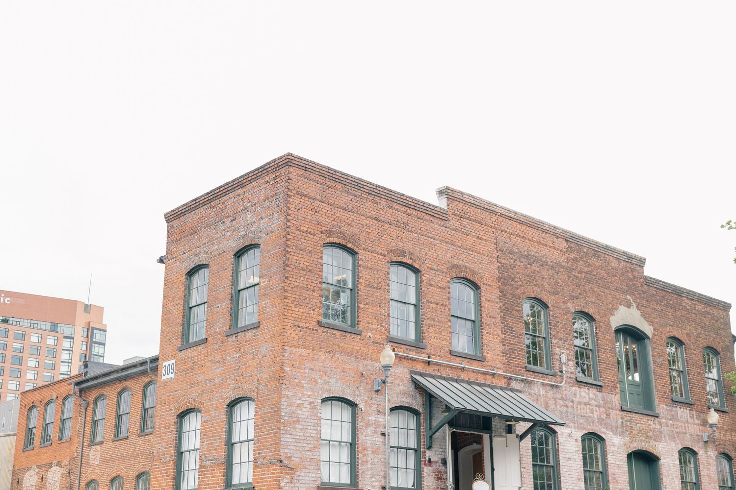 Historic two-story red brick building with green-trimmed arched windows in an urban wedding venue setting.