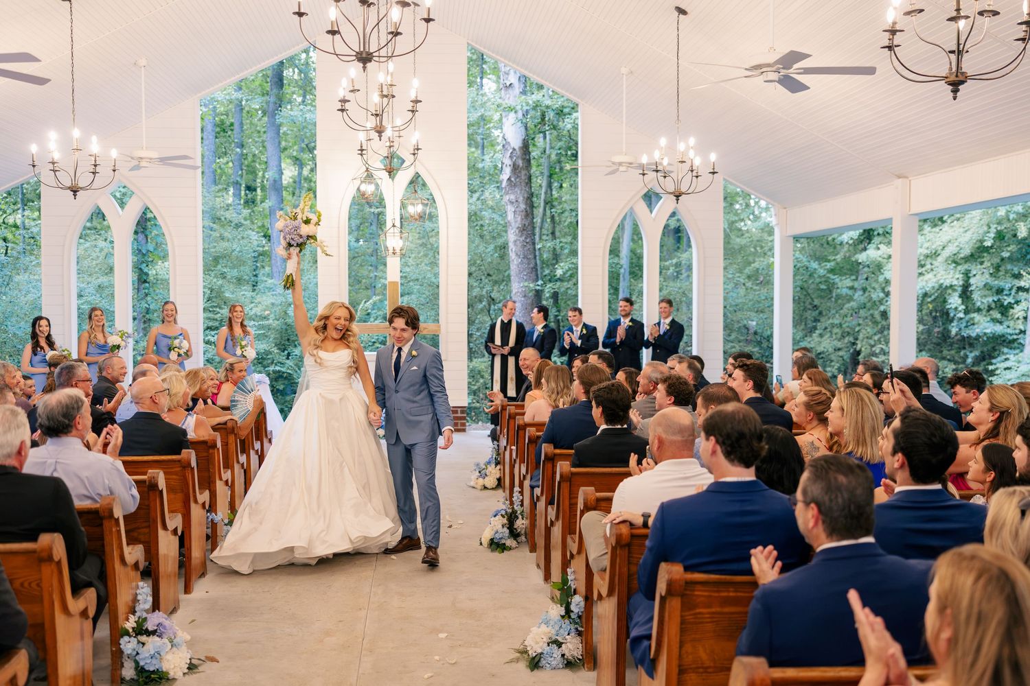 Bride and groom walk down the aisle after wedding ceremony in a stunning glass chapel with arched windows.