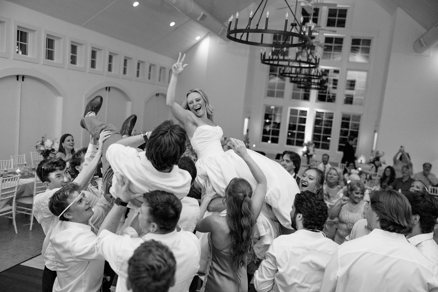 Bride being lifted by groomsmen during a lively wedding reception celebration in a black and white photo.