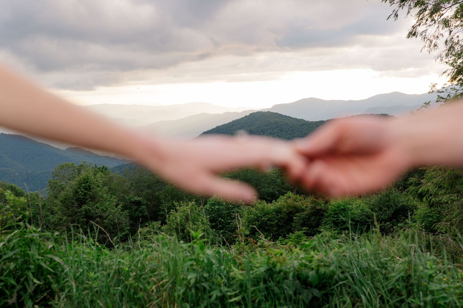 Silhouetted hands reach toward each other against a backdrop of misty mountain peaks at sunset.
