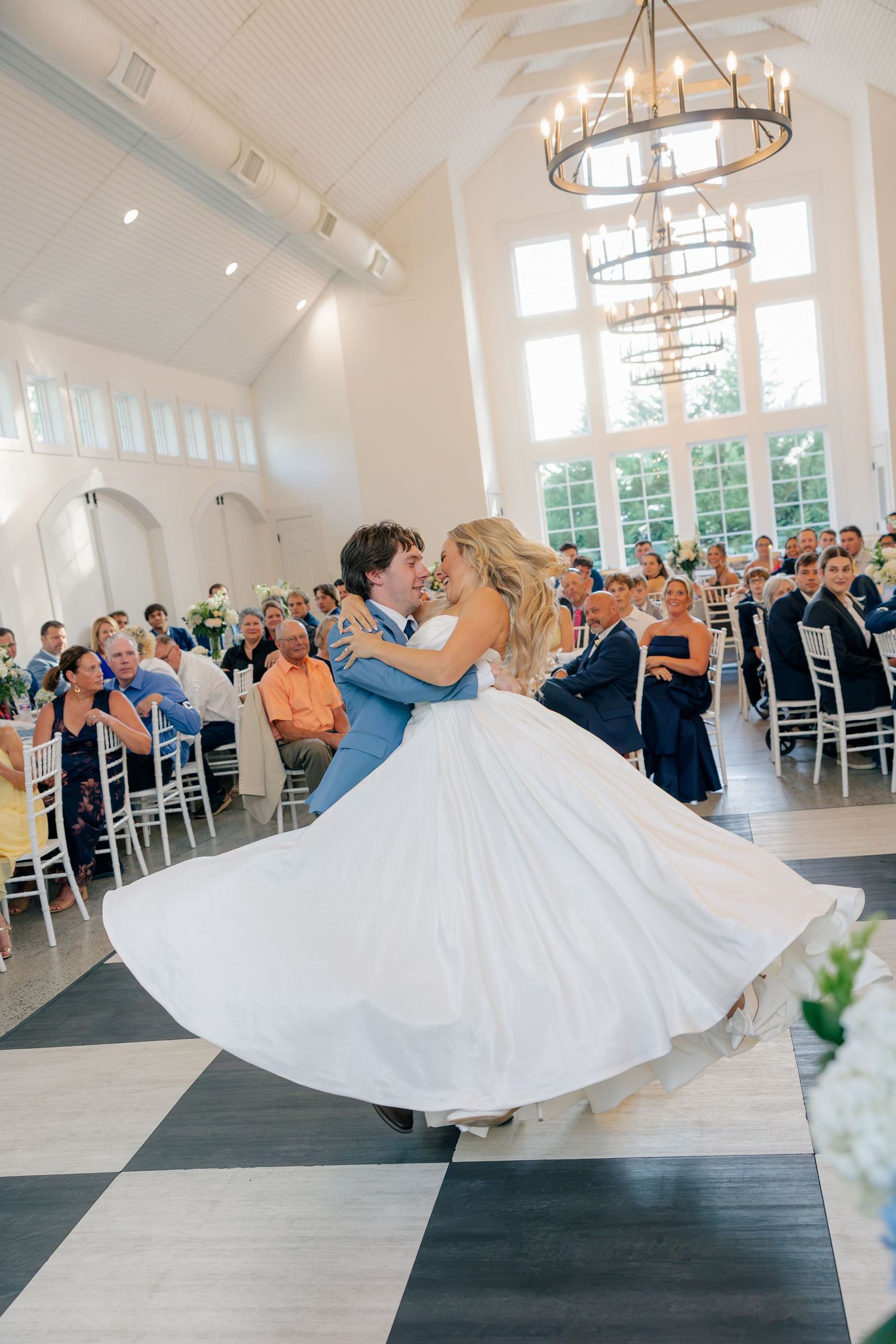 Bride and groom share first dance as dress swirls in bright ballroom.