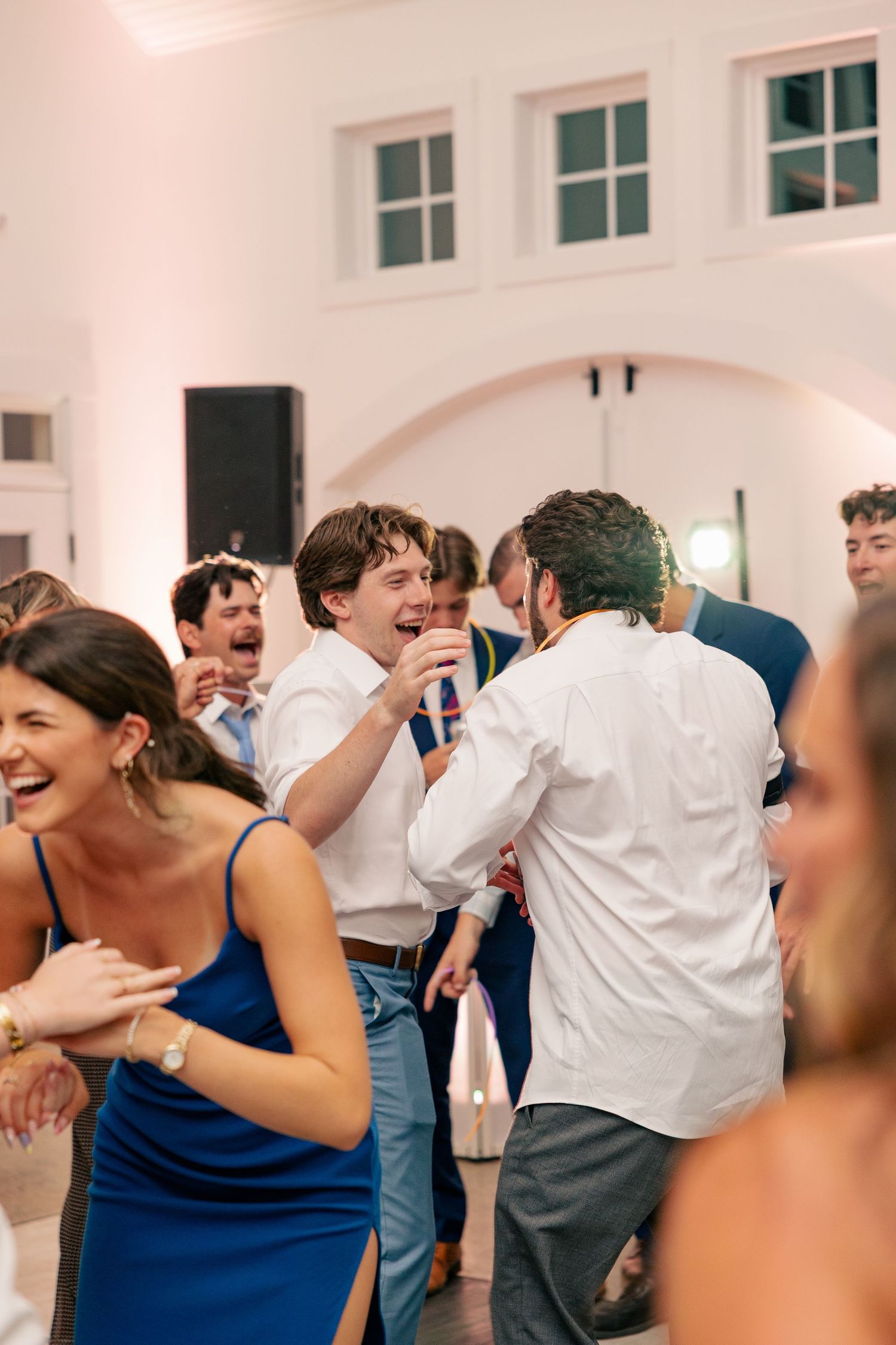 Wedding guests laugh and sing with a microphone on a lively dance floor during the reception.