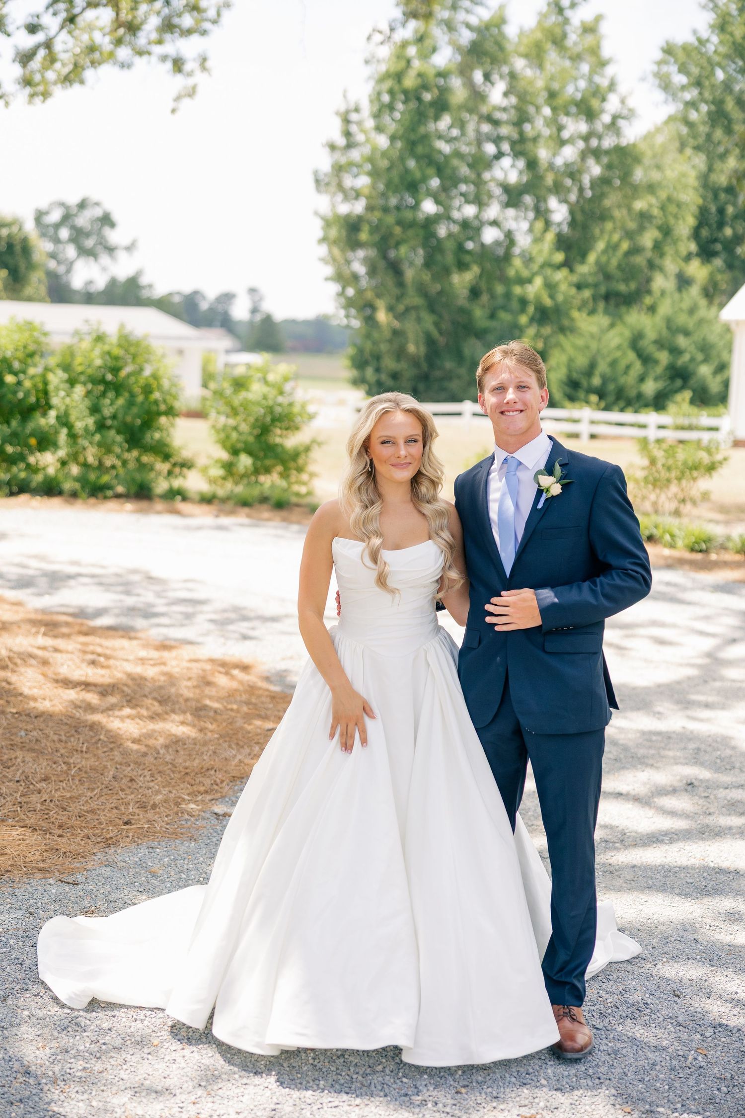 Smiling bride and groom posing together outdoors on a sunny day at their wedding venue.