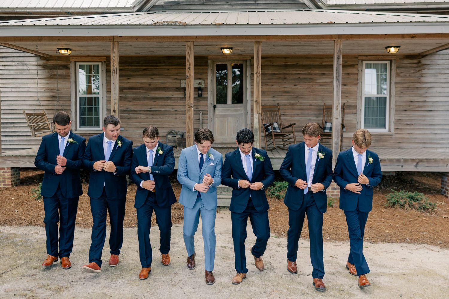 Groomsmen in navy suits walking together outside a rustic wooden building before the wedding.