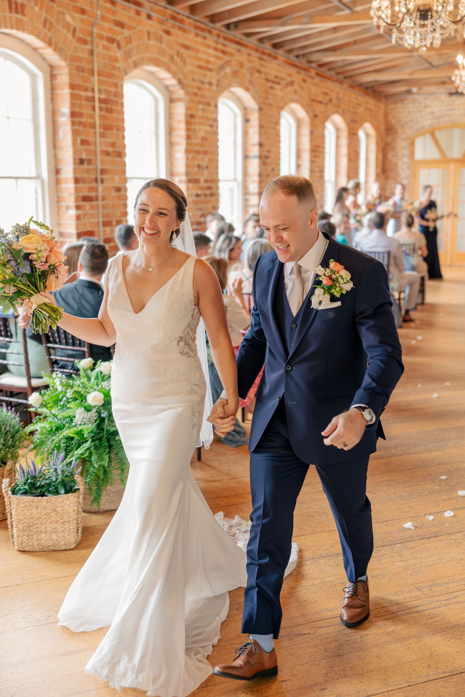 Joyful bride and groom walk back down the aisle after wedding ceremony in a stunning rustic brick venue.