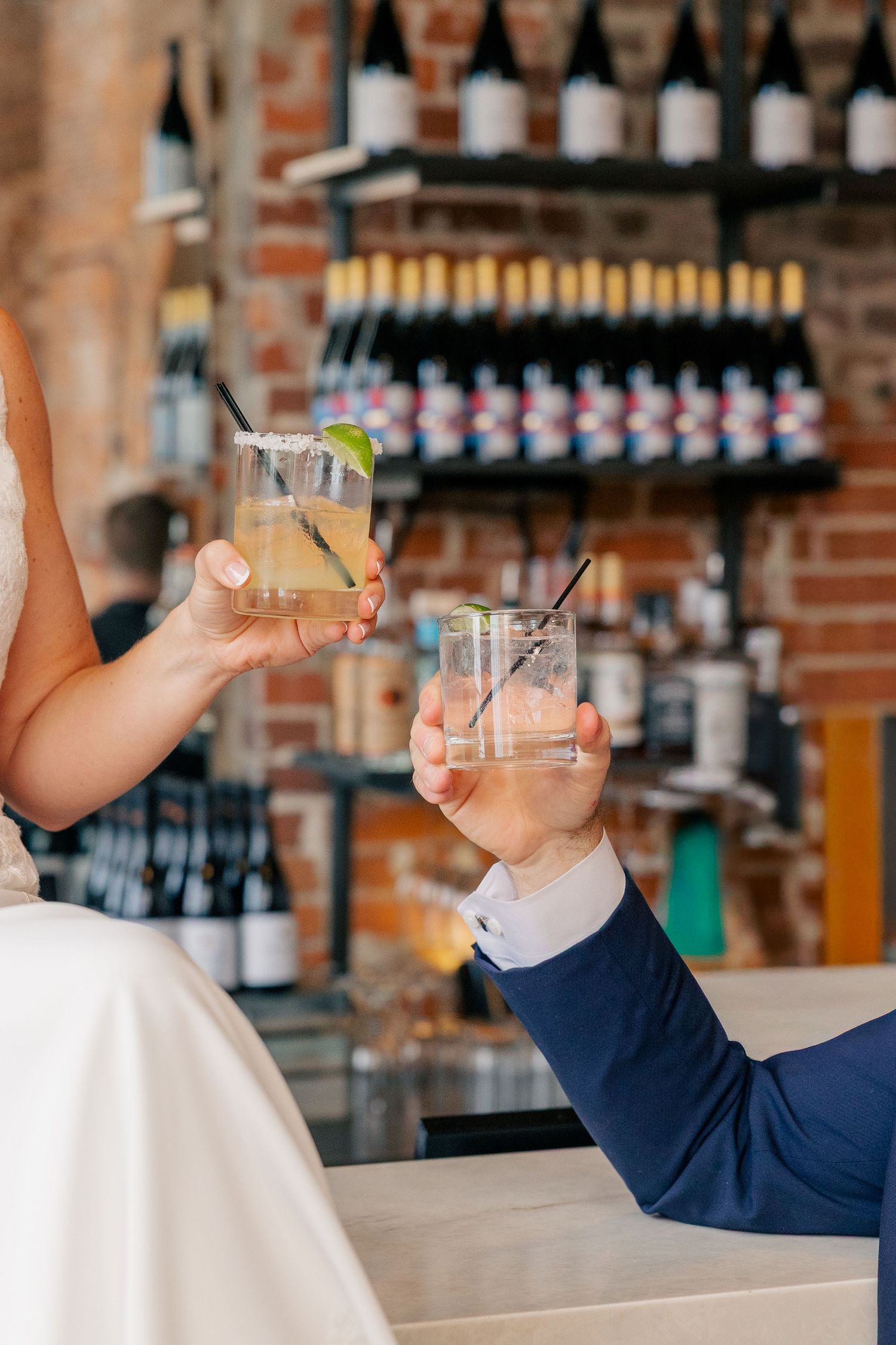 Bride and groom clink cocktail glasses with lime garnish at bar during wedding reception.